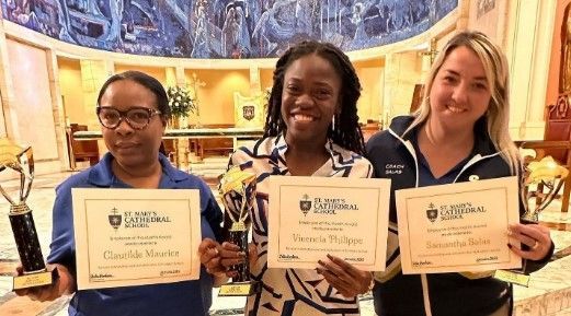 Three women are holding trophies and certificates in a room.