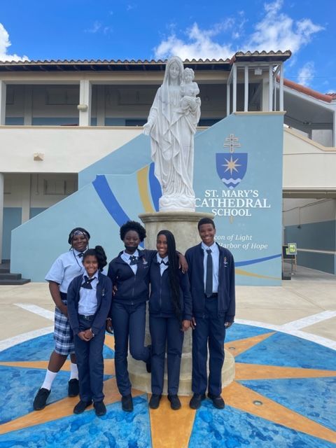 A group of young people are posing in front of a statue in front of st. mary 's cathedral school