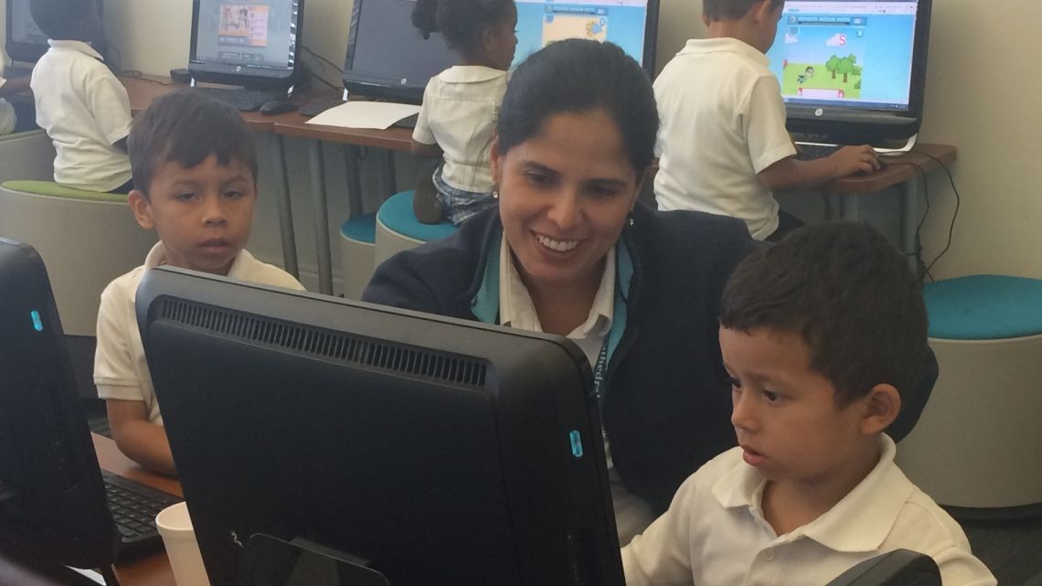 A woman is teaching a group of children how to use a computer