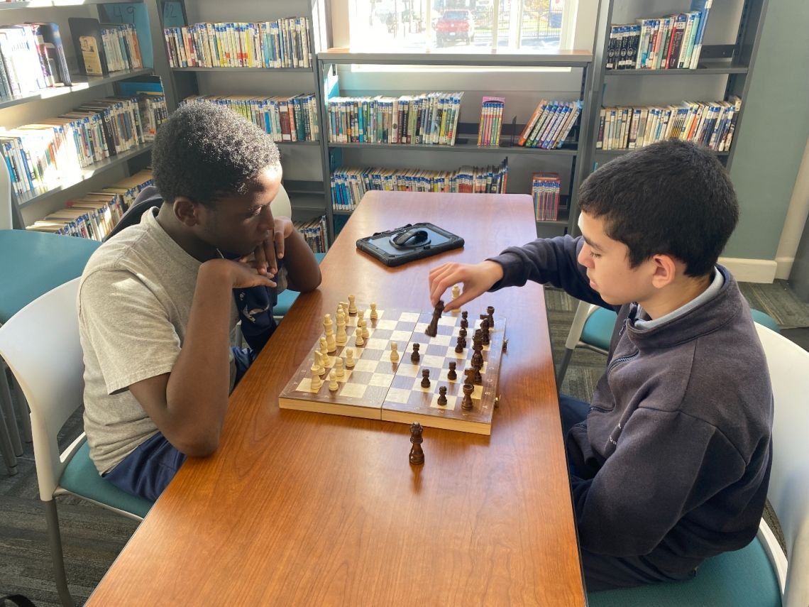 Two boys are playing a game of chess in a library