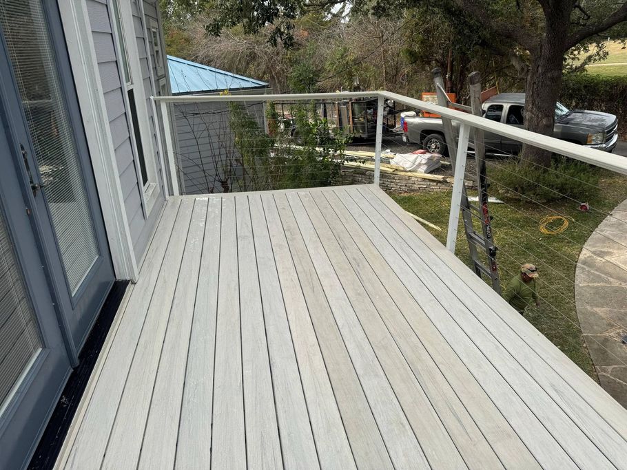 A gray wooden deck with white railing, viewed from a doorway, overlooking a yard with a parked truck and a blue shed.