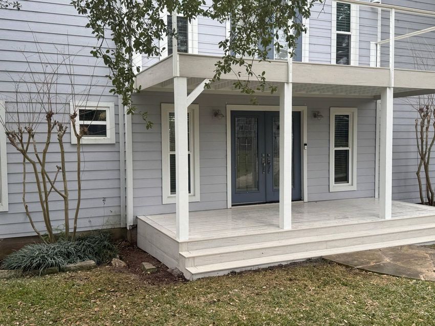 A light gray two-story house with a wooden porch, double doors, and a balcony.