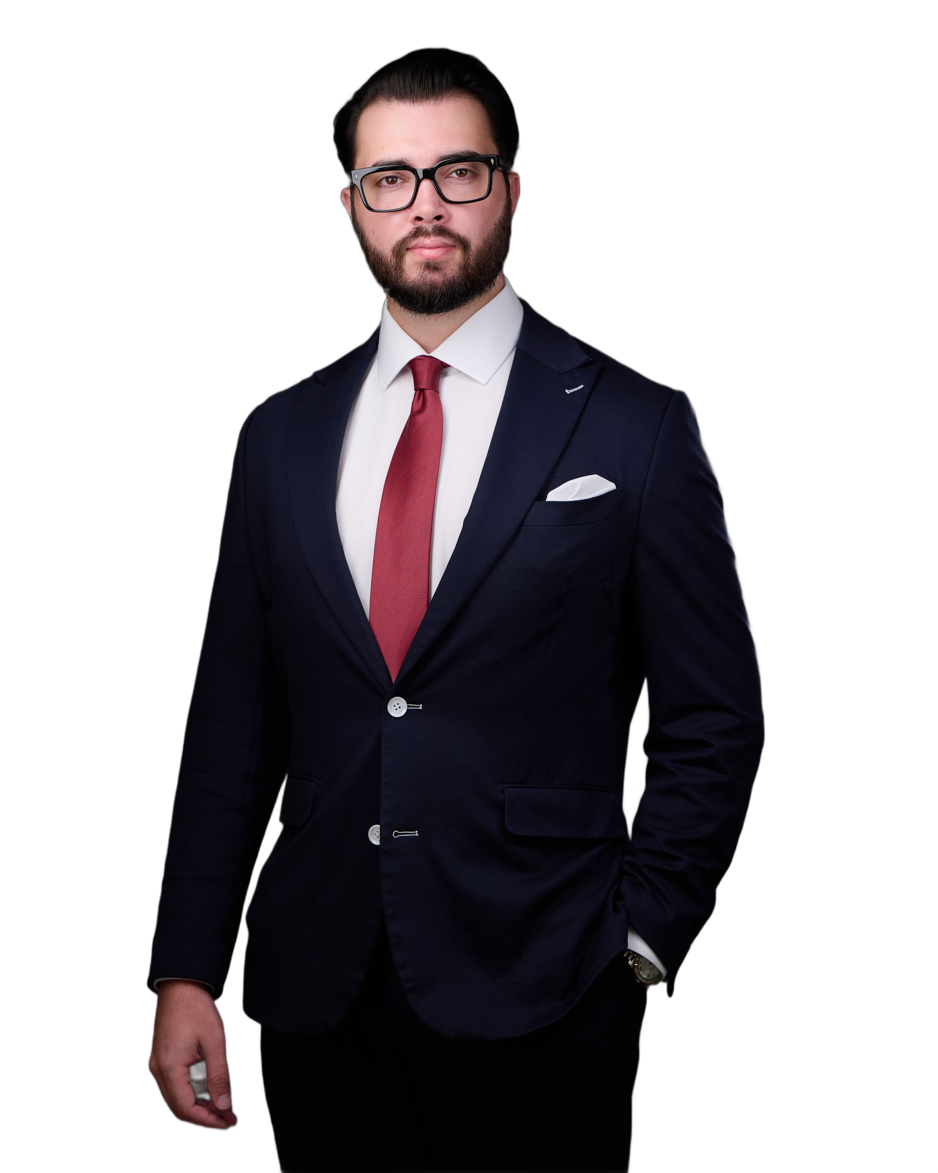 Man in a navy suit with a red tie, wearing glasses, and a white pocket square, standing and looking at the camera.