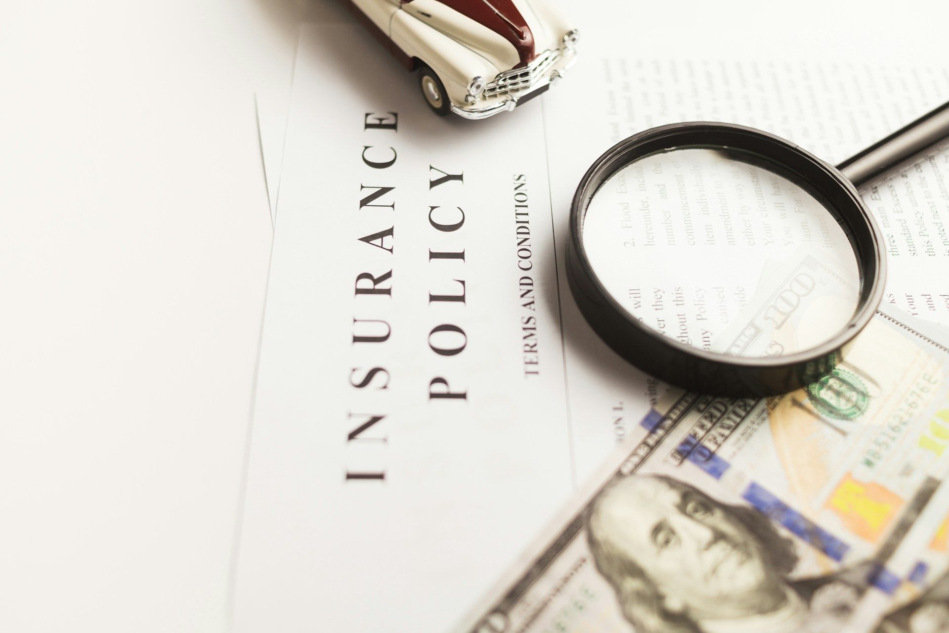 Insurance policy document with toy car, magnifying glass, and cash.