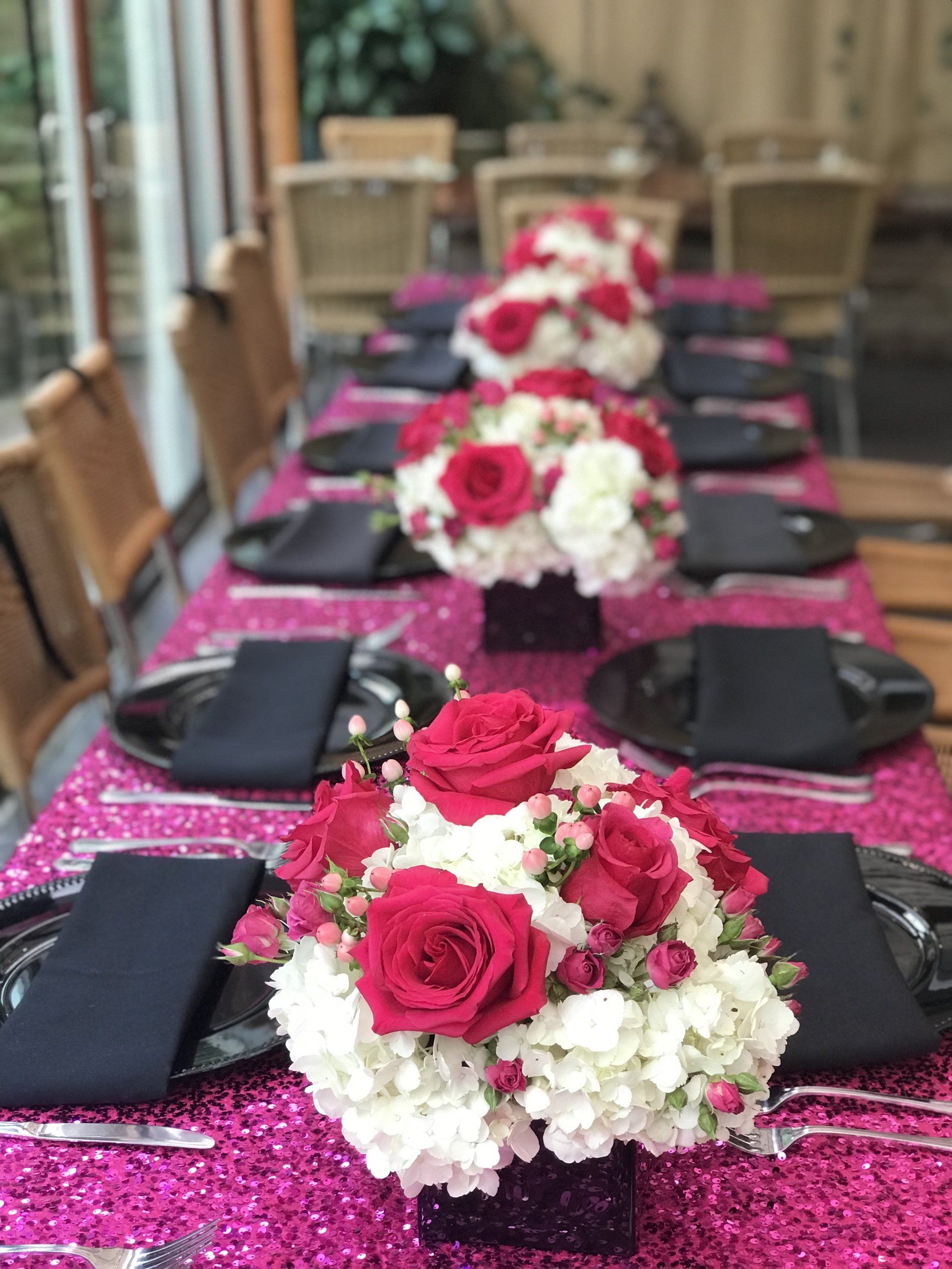 Long table set up with multiple floral centerpieces, a sequin table cloth and black plates and napkins.