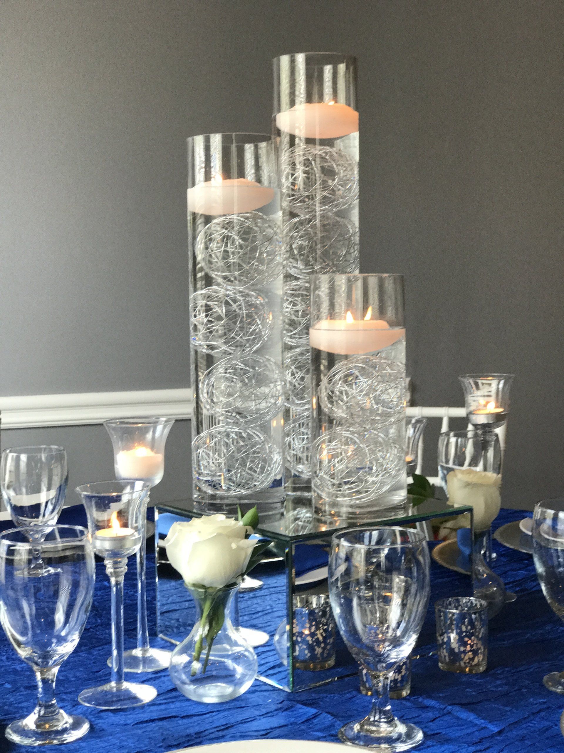 Elegant centerpiece with three cylinder floating candle holders of varying heights sitting on a mirrored raised base.