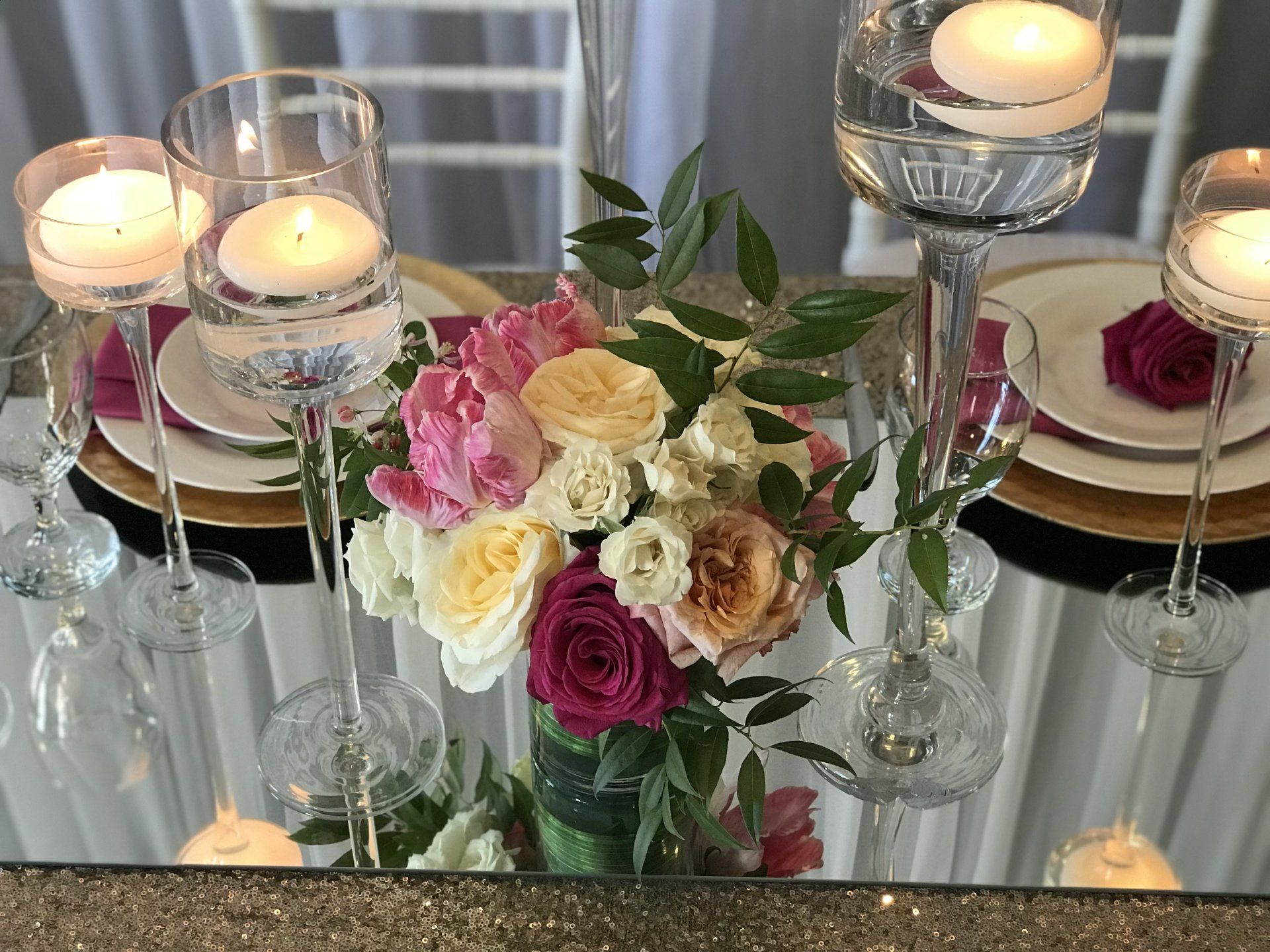 Beautiful centerpiece consisting of a floral arrangement with tall stem floating candle holders sitting on a mirror.