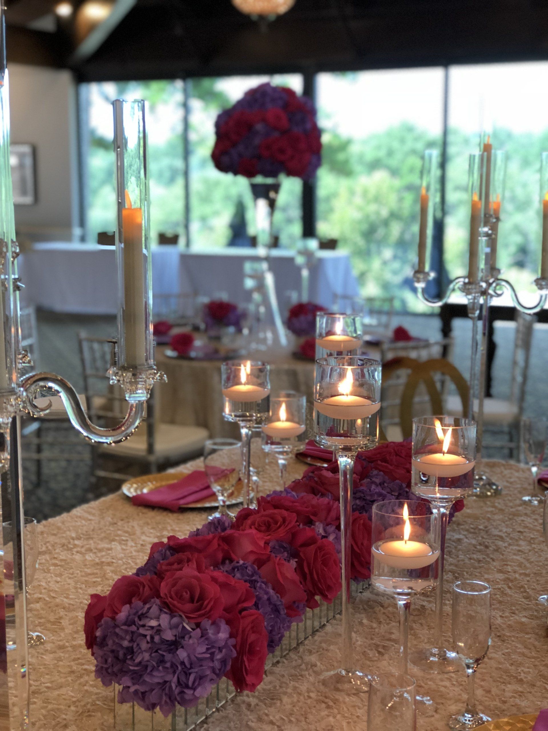 Event table setup with floral centerpieces, tall stem floating candle holders and clear candelabras.