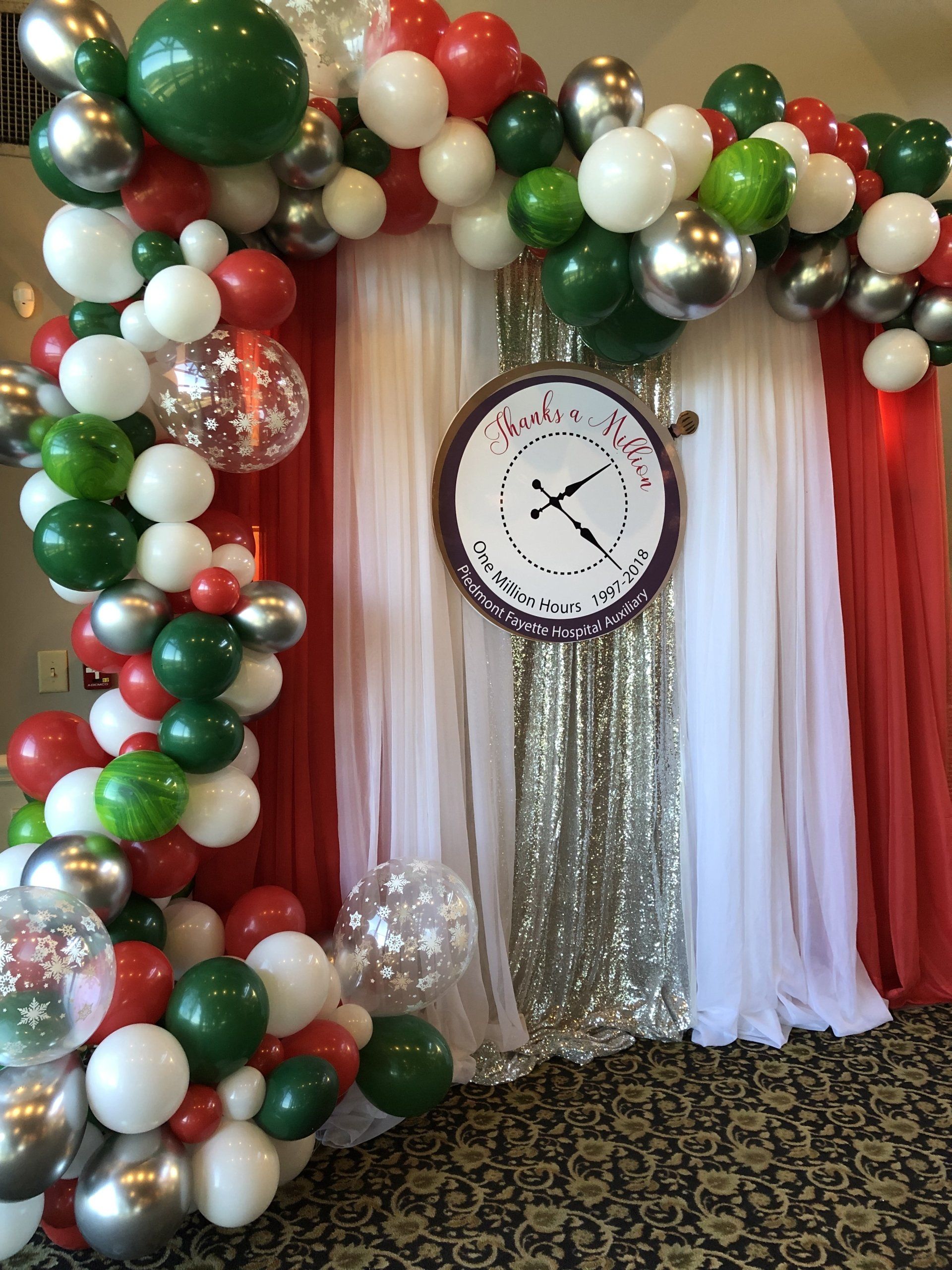 A festive and colorful organic balloon garland adorns a beautiful backdrop with a sign in the middle.