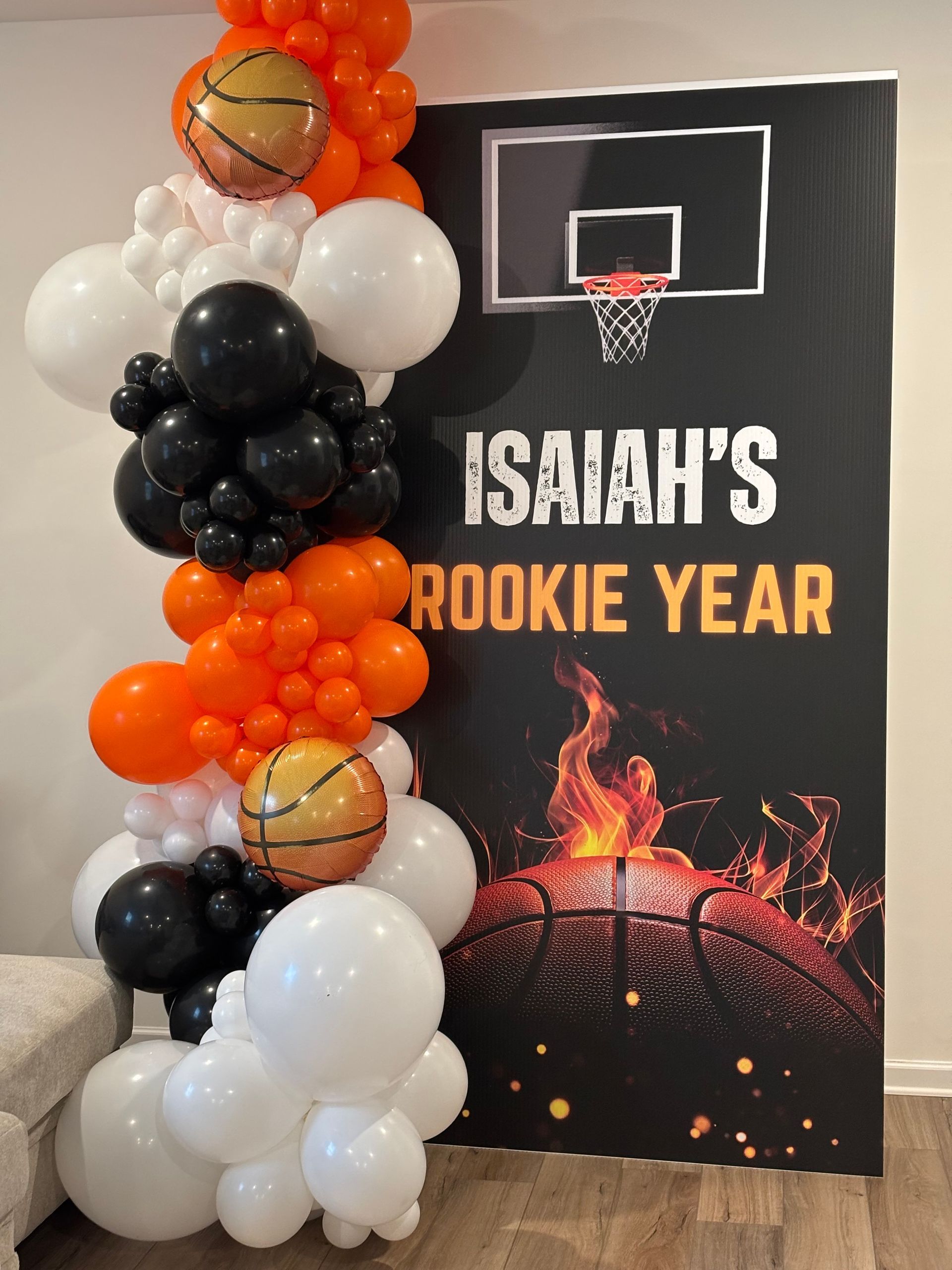 Basketball themed birthday backdrop with hoop graphic and black, orange, and white balloon garland for kids sports party