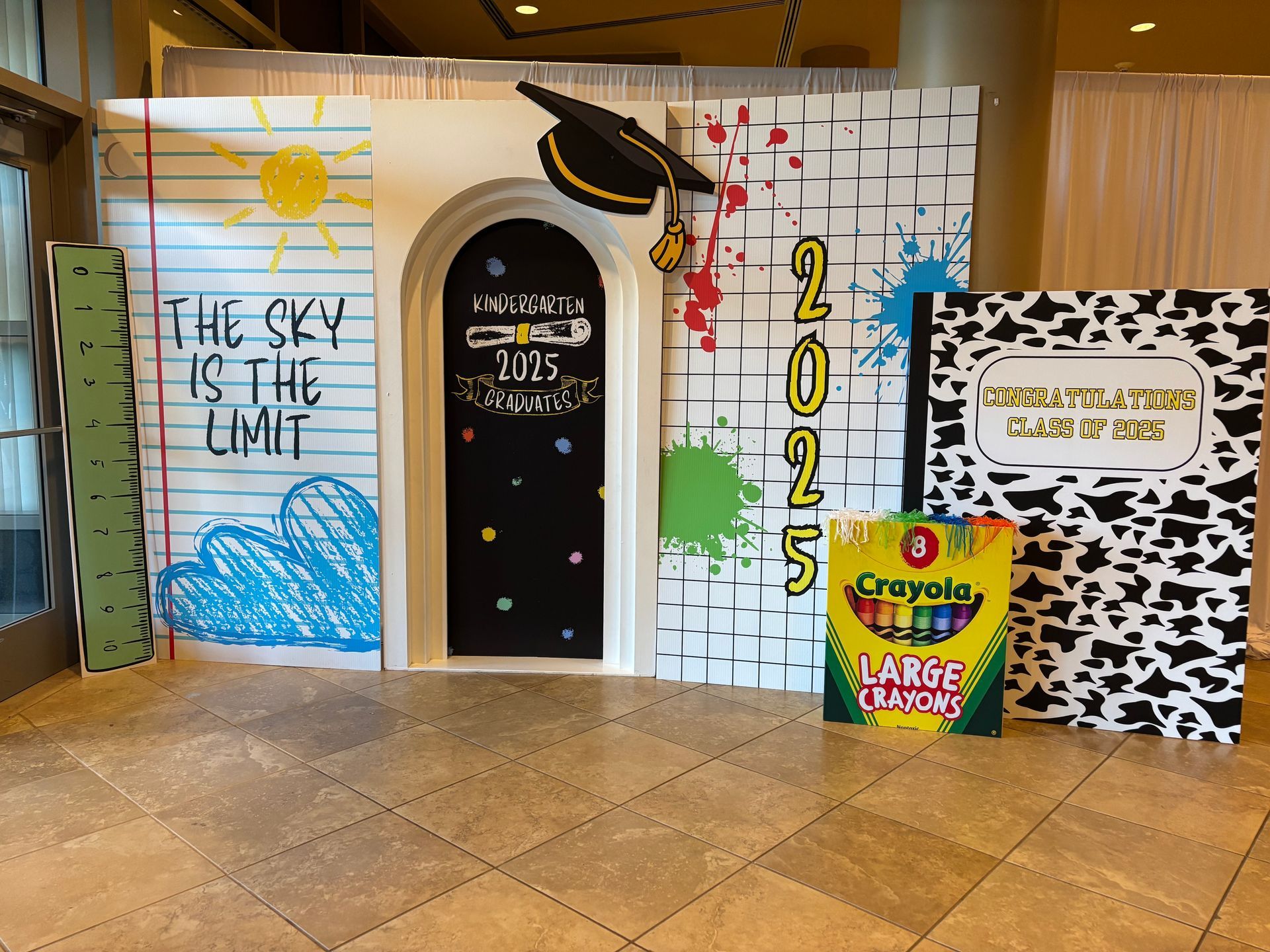 School themed graduation backdrop with classroom door props, crayons, and 2025 decor for kids milestone celebration