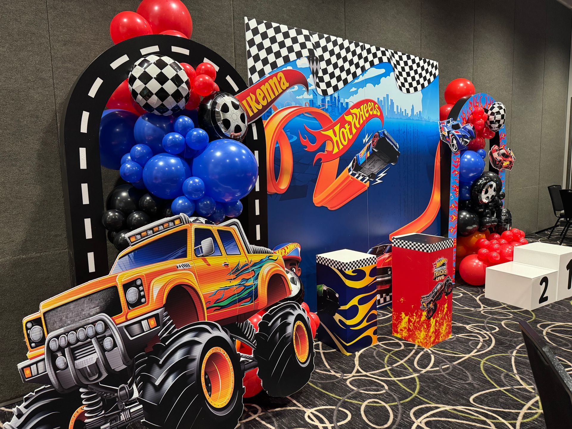 Race track themed kids birthday setup with Hot Wheels backdrop, balloon arches, and toy car props for photo booth