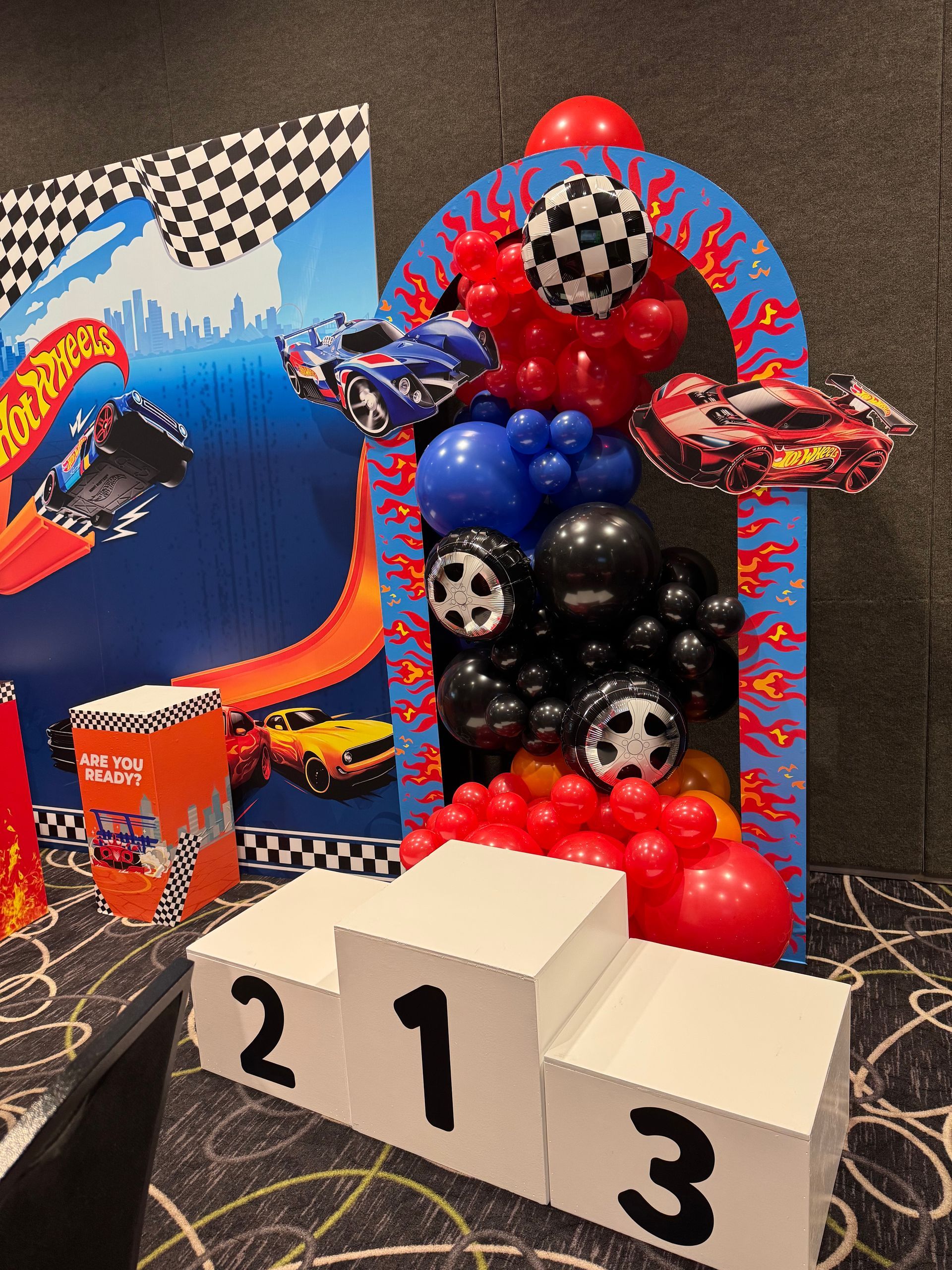 Hot Wheels themed balloon backdrop with race cars and checkered flags for boys racing birthday party