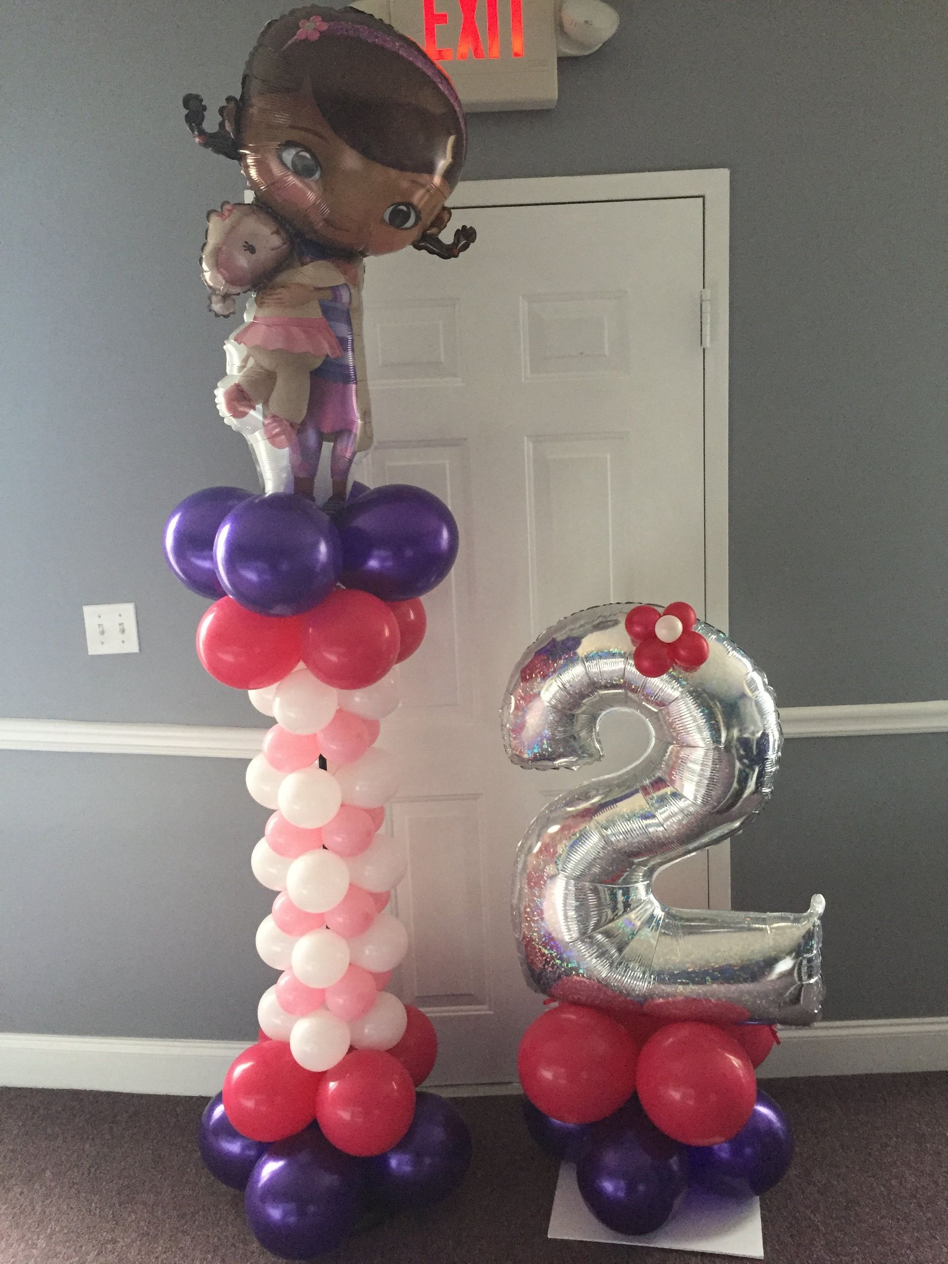 Two columns, both comprised of balloons. One is tall with Doc McStuffins at the top and the shorter one has the number 2 on top of a small bed of balloons.