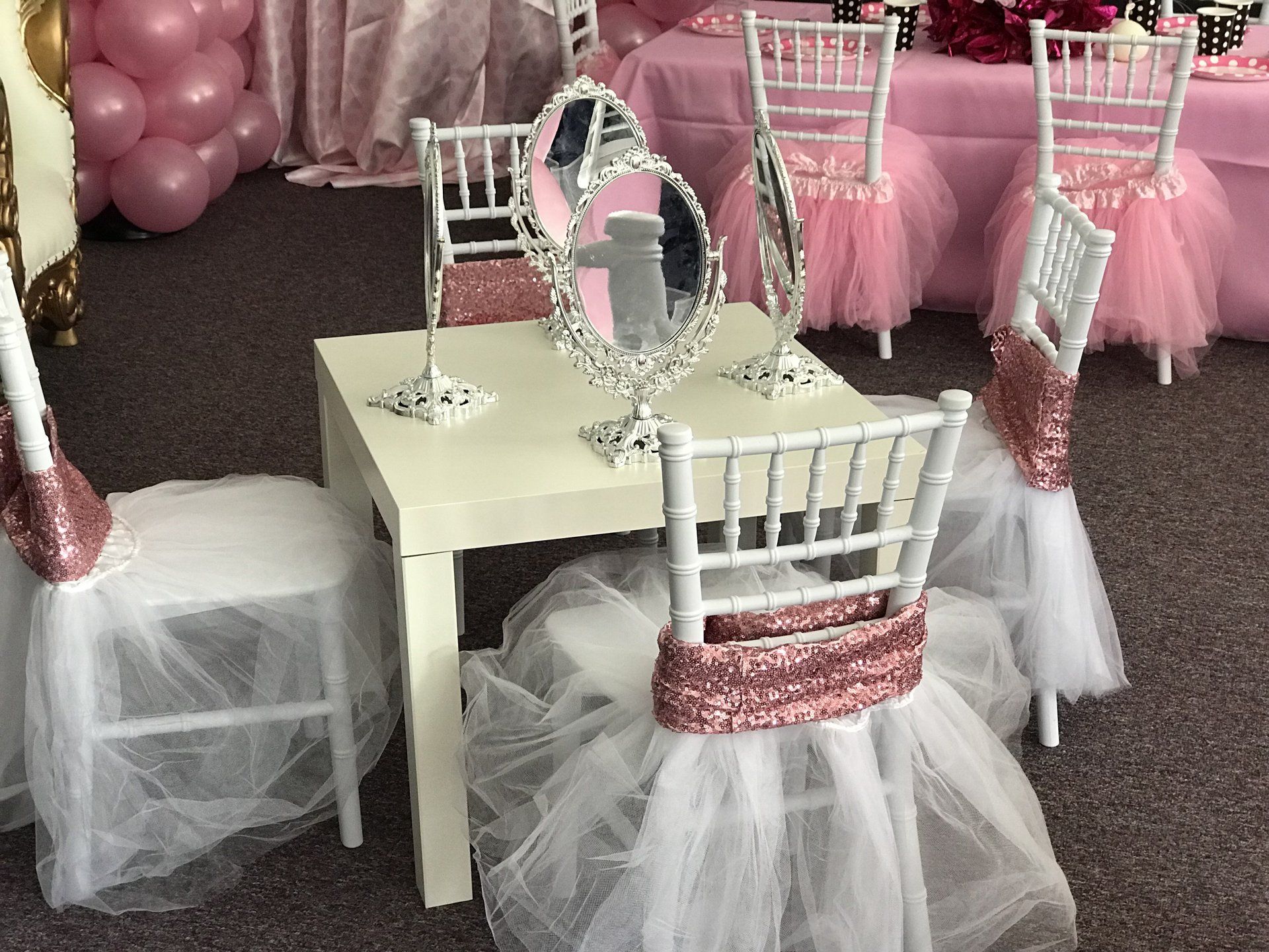 Side table at a girls birthday party will a mirror at each of the four chairs. Chairs are decorated with a sequin pink wrap and a tulle skirt.