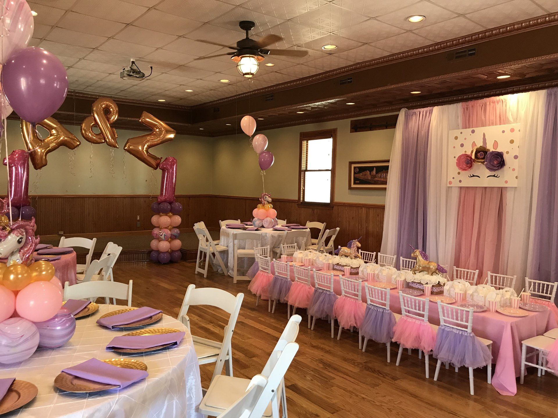 Overview of custom kids event design. One long table with pipe and drape in the back, three rounds, and a large balloon display.