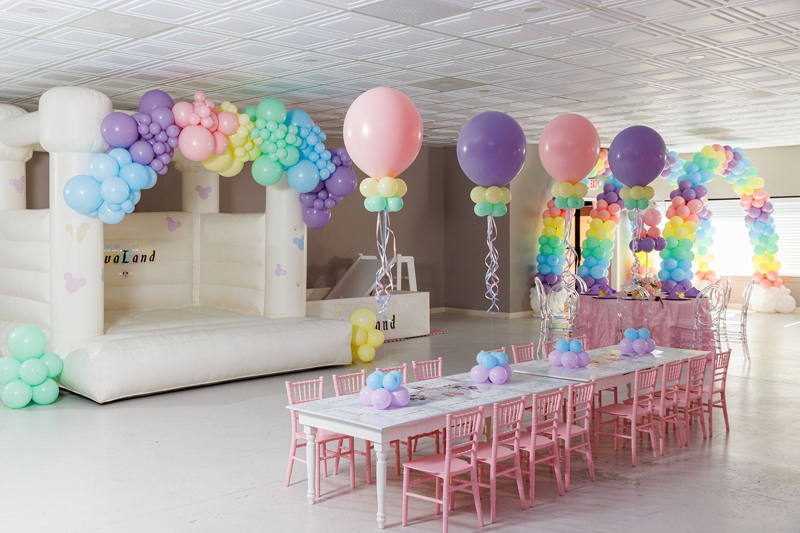 White bounce house rental decorated with pastel rainbow balloon arch for kids birthday celebration