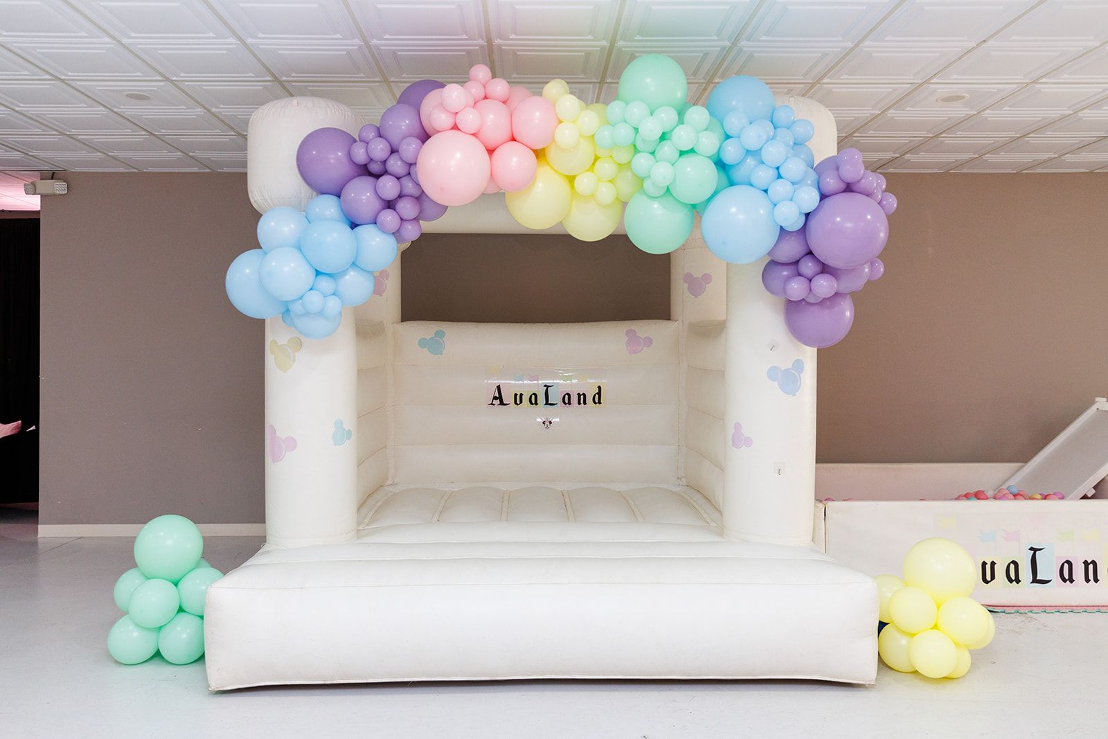 Inflatable kids bounce house with soft pastel balloon garland and custom name banner for birthday party