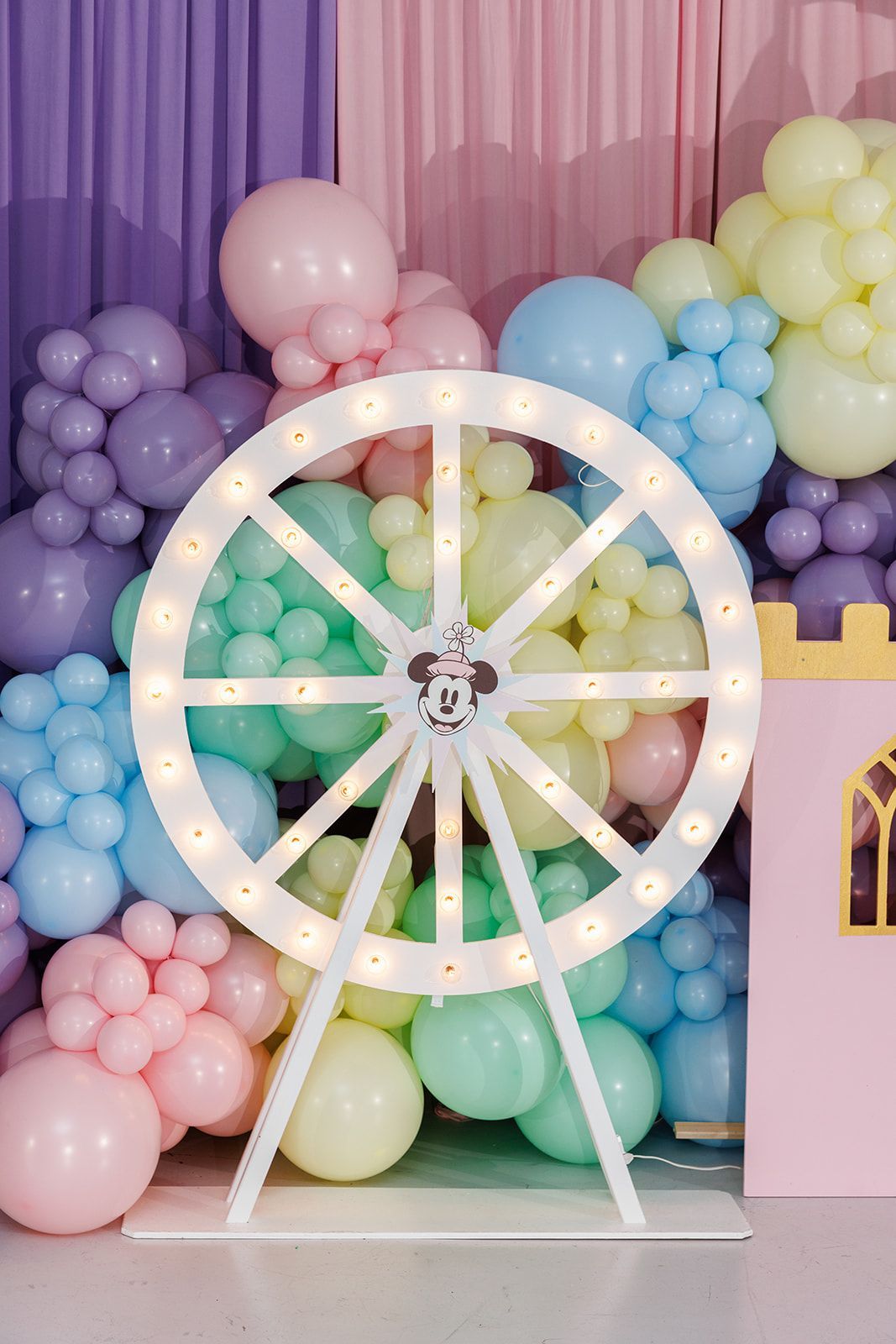 Close-up of pastel balloon clusters with purple and pink draping and decorative light-up ferris wheel prop