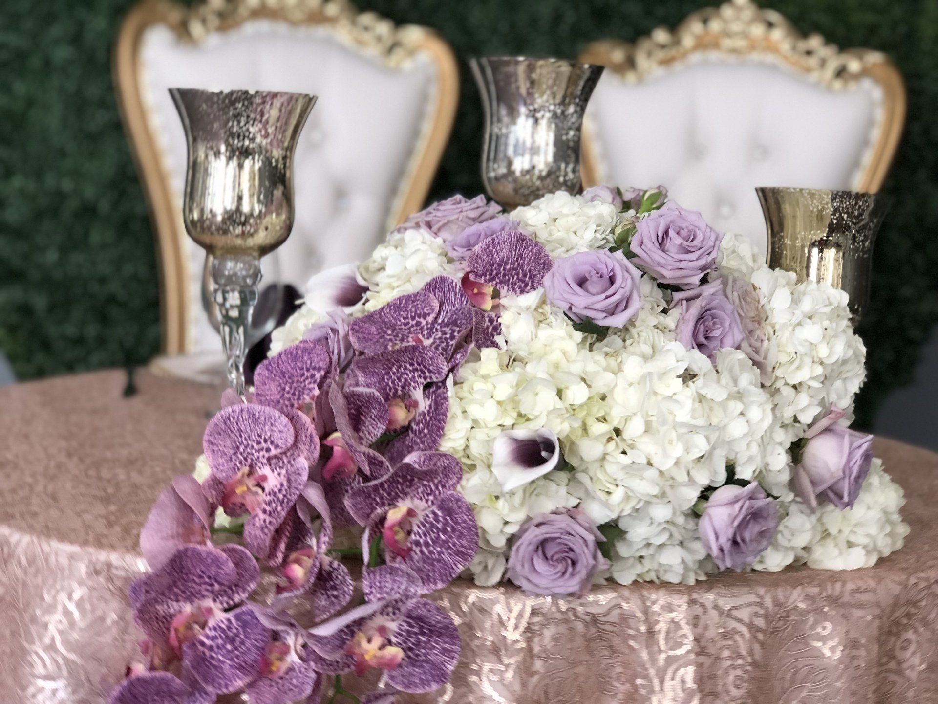 A gorgeous cascading floral centerpiece with purple orchids, roses and more. Elegant long stem candle holders are in the background.