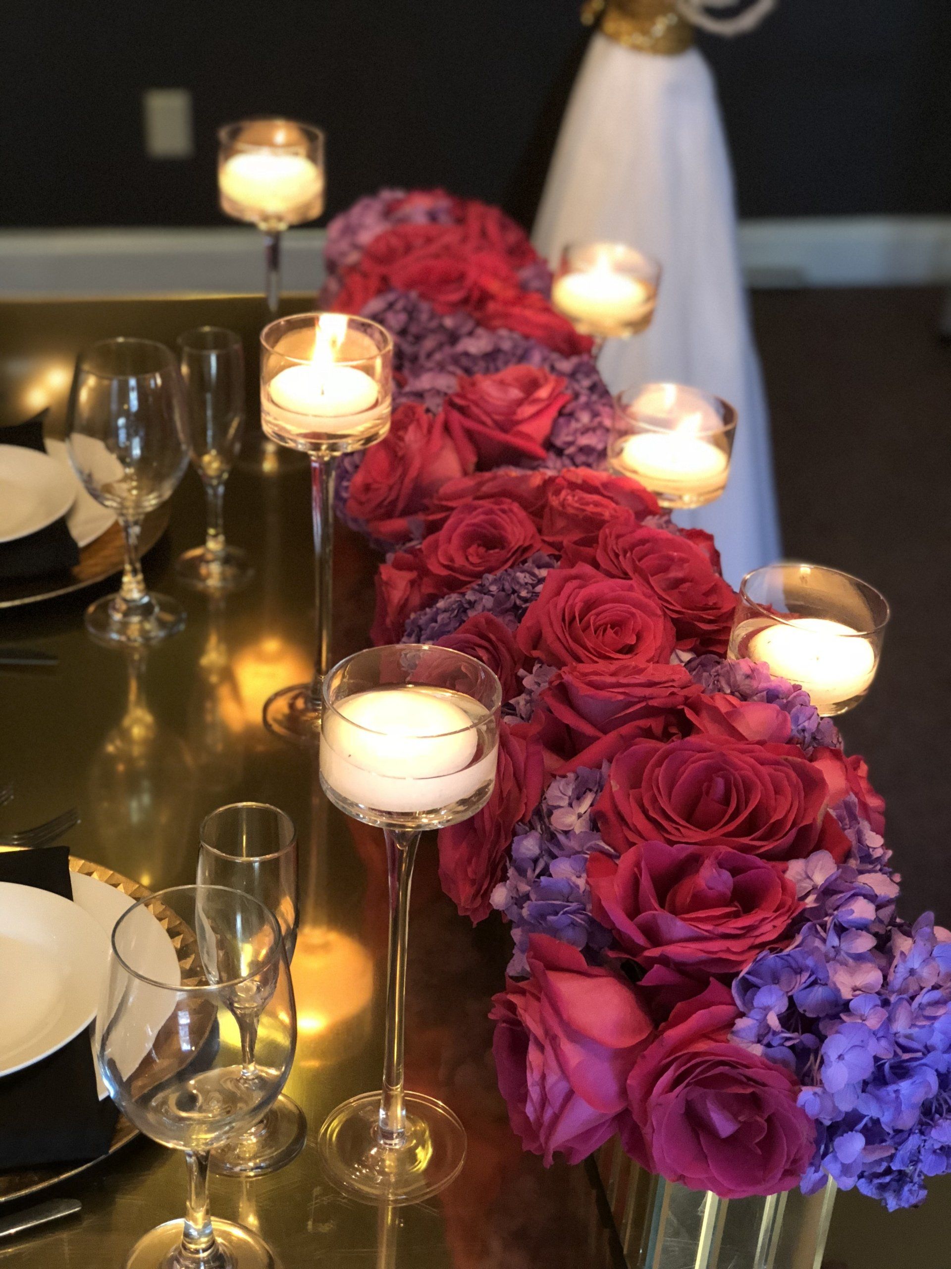 Table setup with floating candles in glass candle holders, a floral centerpiece and gold chargers.