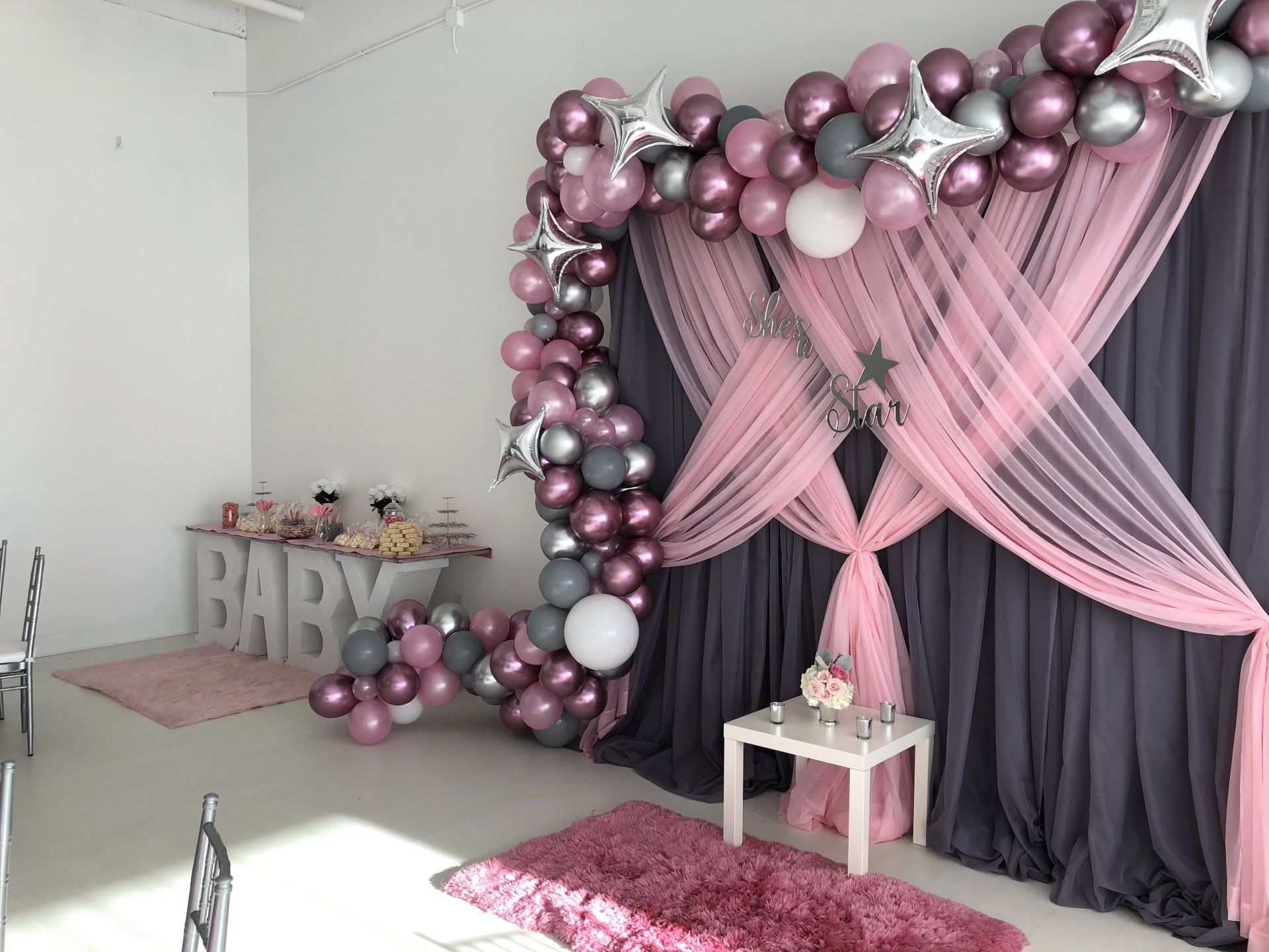 A backdrop for a baby girl's shower framed with a balloon garland.