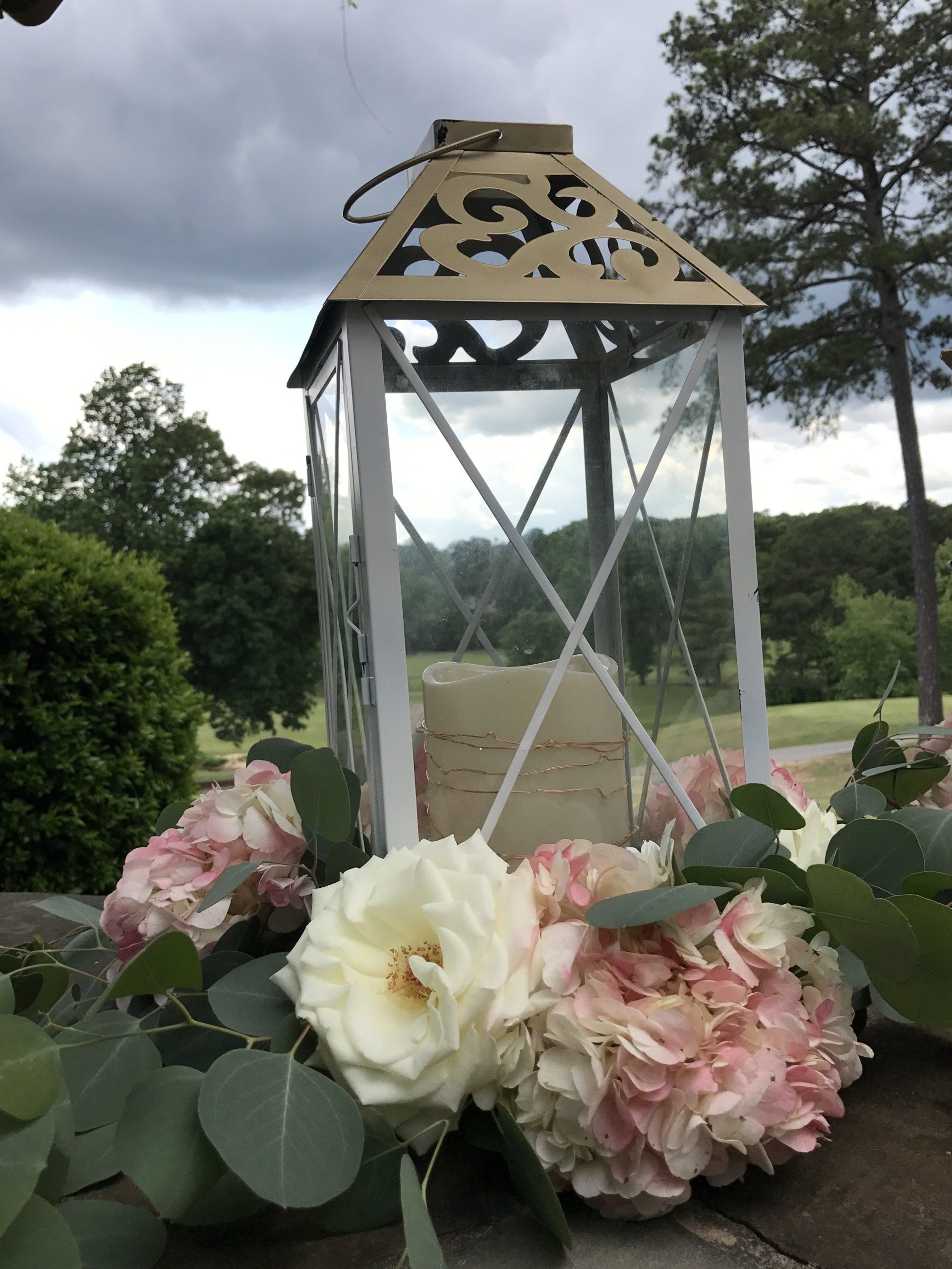 Event decor with white and gold trimmed lantern and a floral accents at the base.