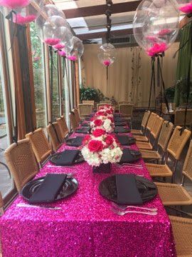 Banquet table with sequin table cloth, floral centerpieces, black chargers and napkins, and balloon design floating from the chairs.