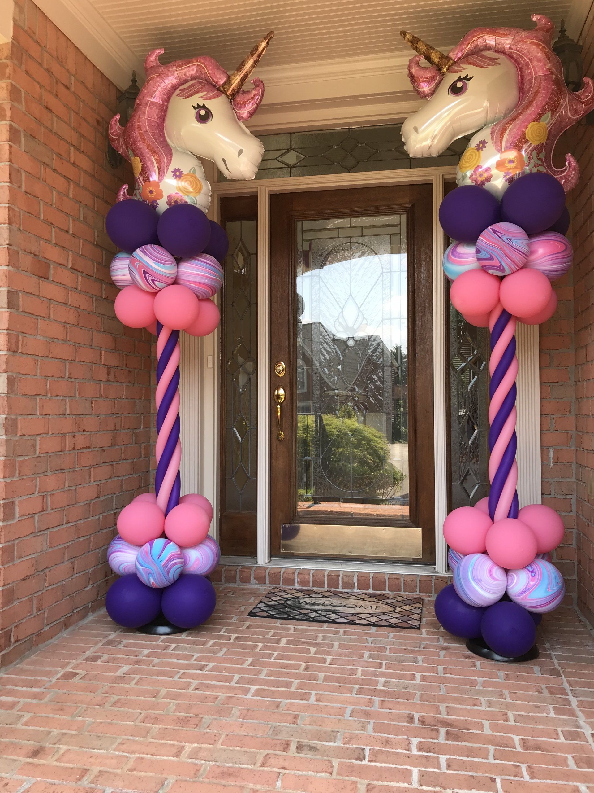 Two balloon columns placed on either side of a doorway. They are created with multiple styles and colors of balloons with unicorns at the top.