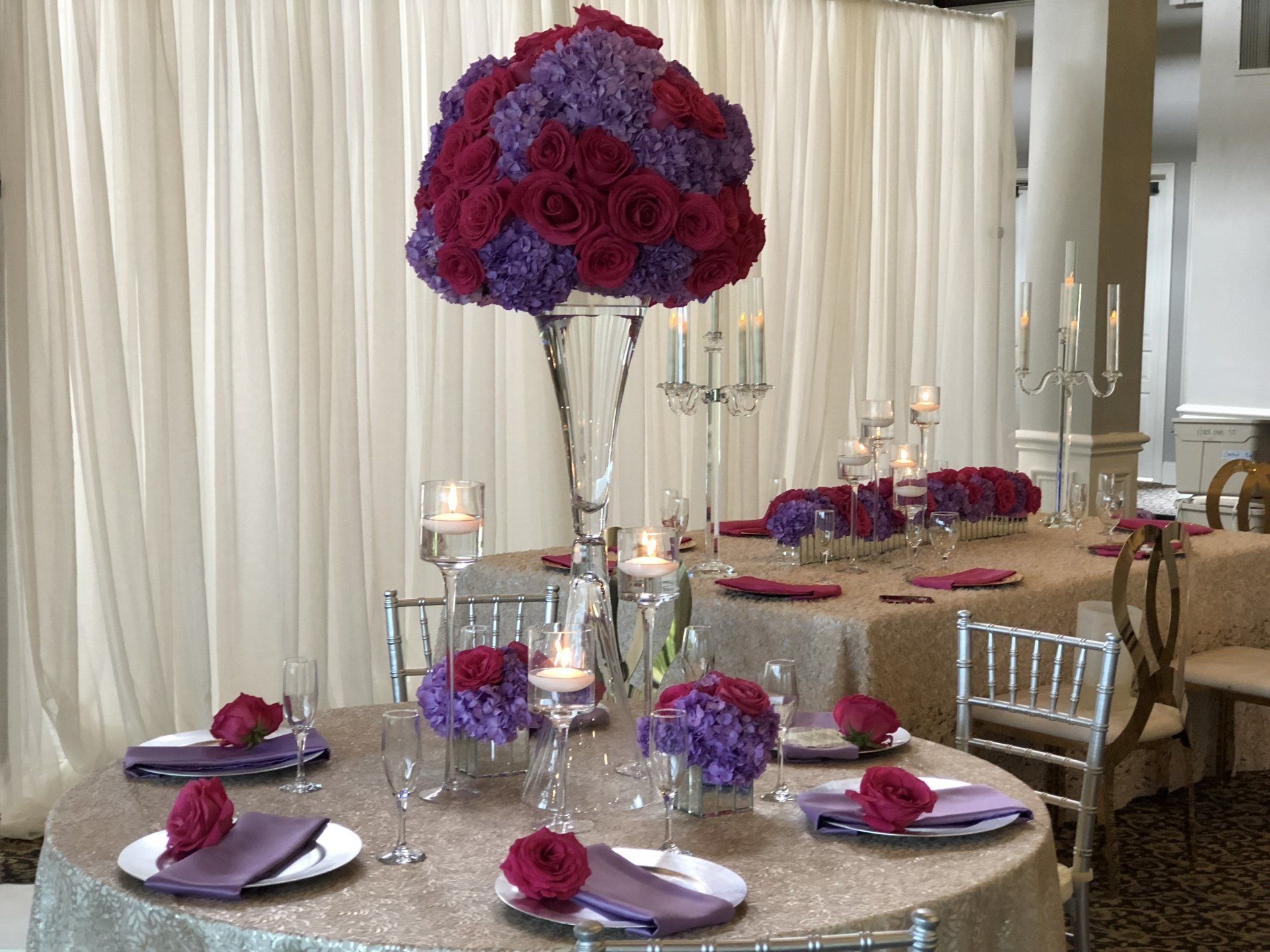 Multi table style event set up. Floral centerpieces with with multiple designs, clear candelabras, and floating candles in long stem contemporary candle holders.