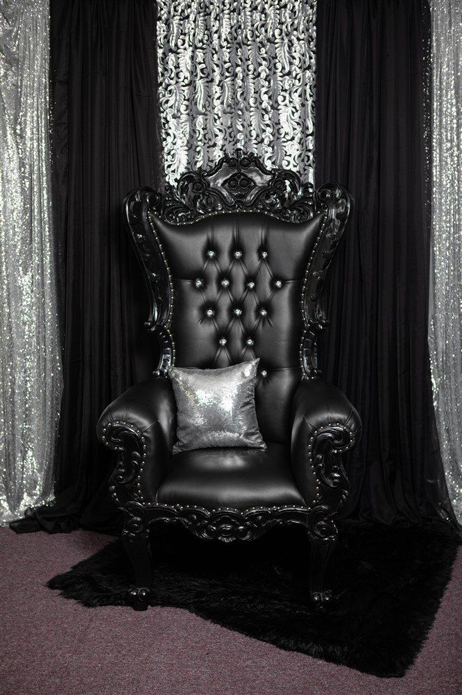 An African throne with black trim and cushions. Multi panel silver and black draping in the background.