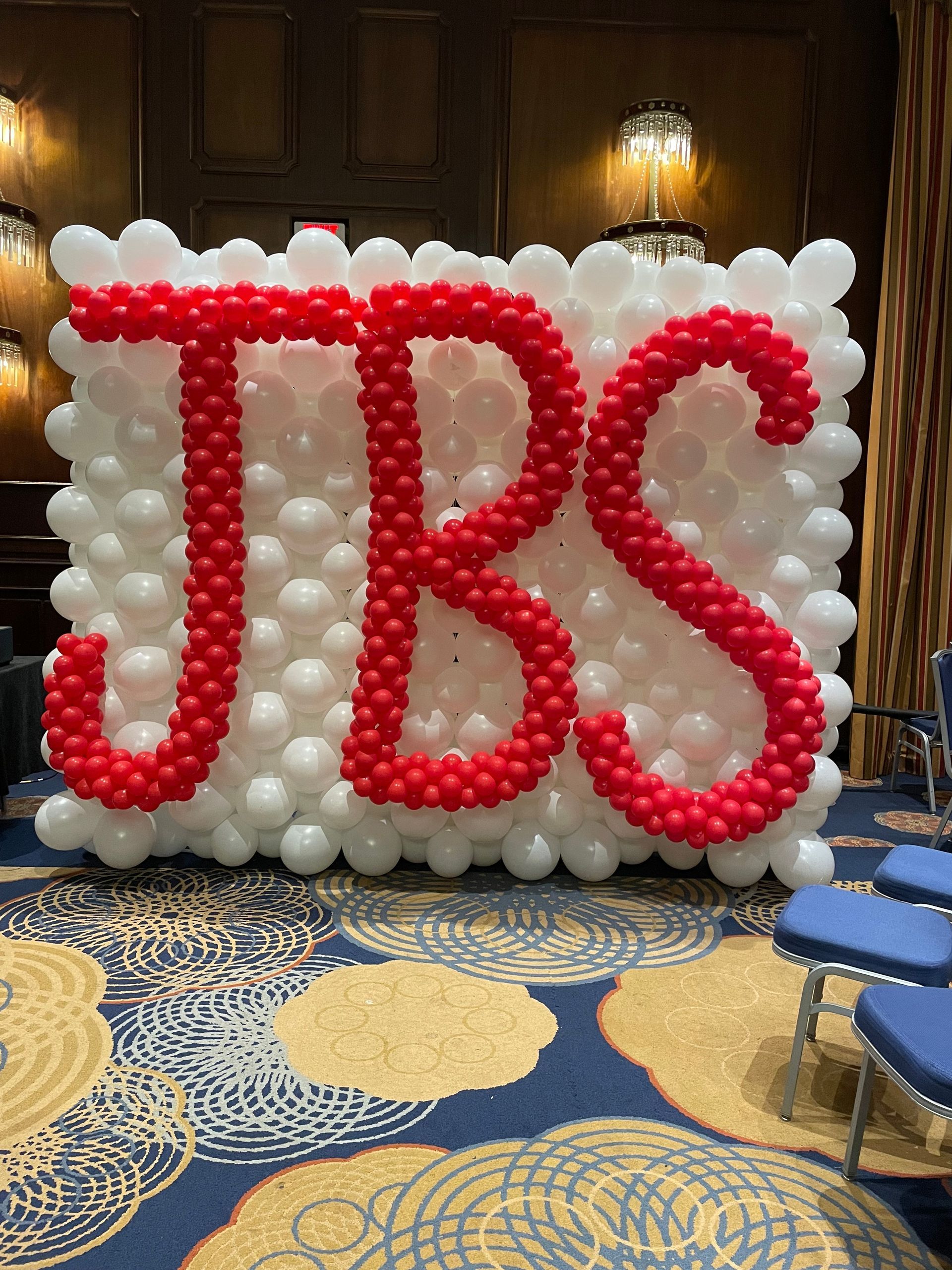 Two columns created with spiraling red and pink balloons and a one and three at the top along with a pink carpet leading up the stairs welcome guests as they arrive.
