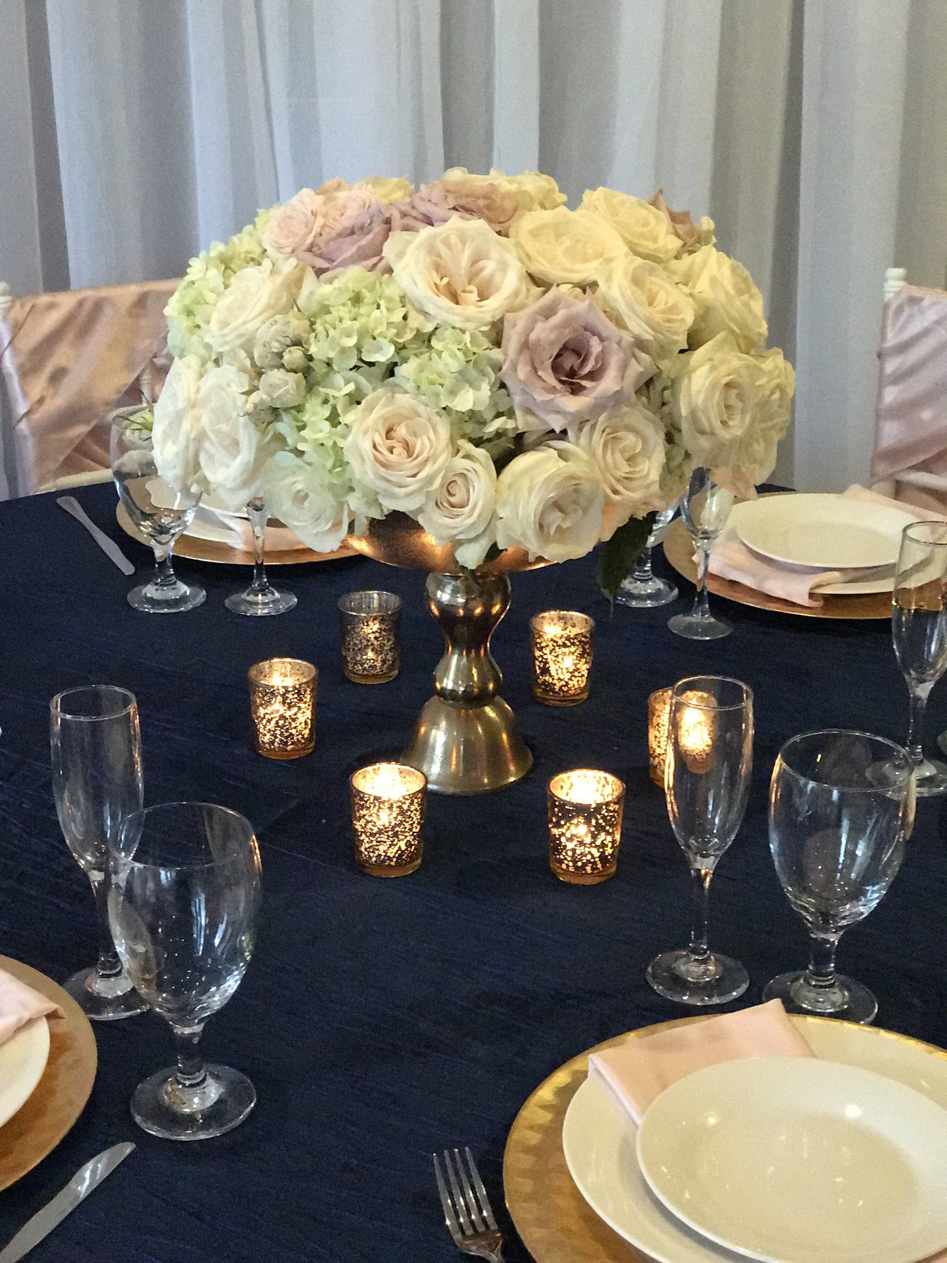 Floral centerpiece in a metal vase and tea light candles surrounding it.