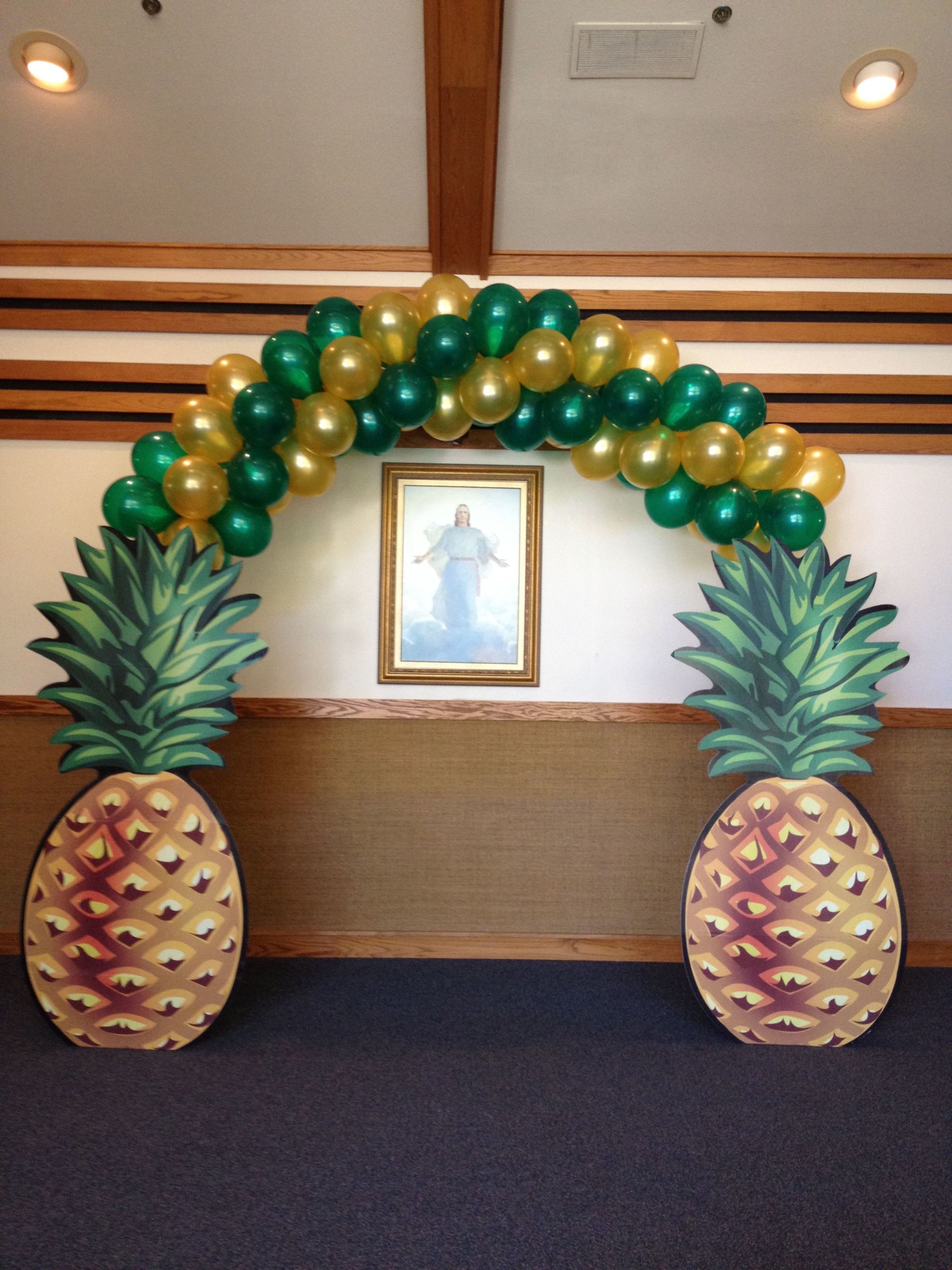 A green and gold balloon archway with large cardboard pineapples as the anchors.