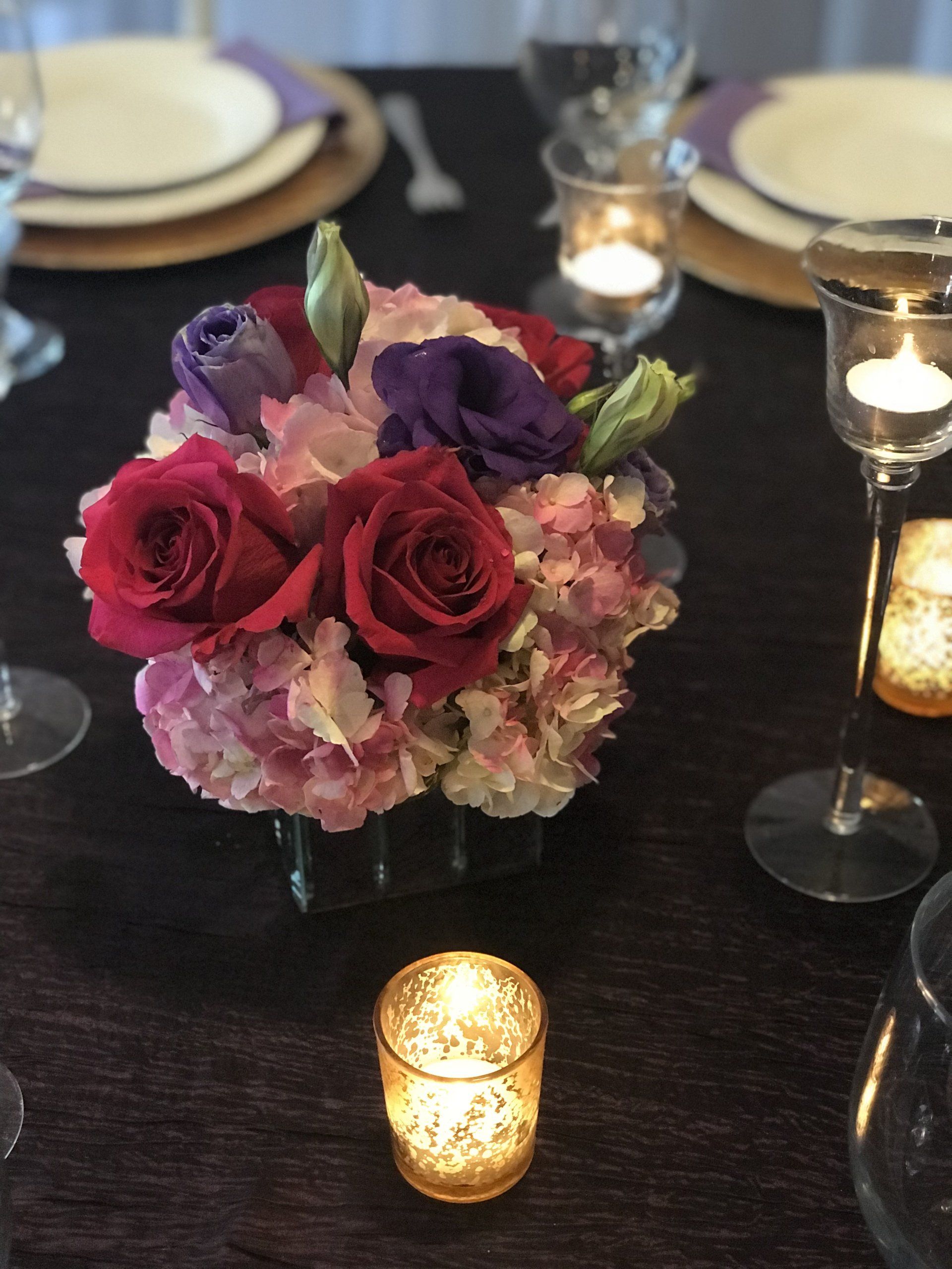 Close up of a floral centerpiece as part of table design with place settings, glasses and candles.