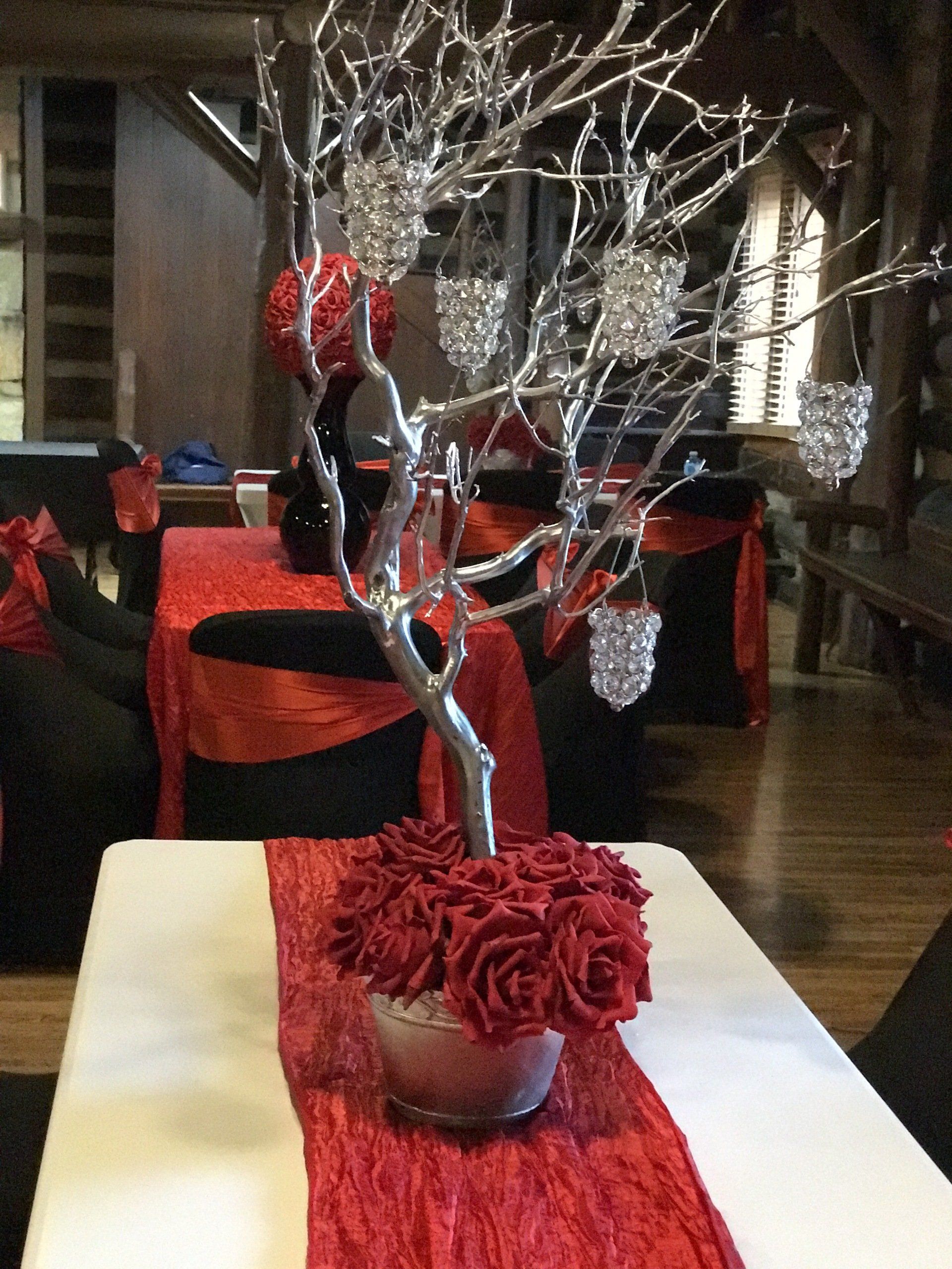 Elegant centerpiece with silver branch, hanging beaded candle holders, and silk roses at the base on a crushed red table runner.