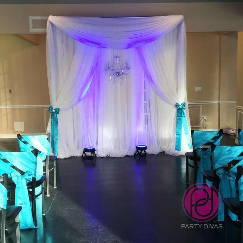 An elegant draped backdrop for a ceremony with a beaded chandelier and uplighting.