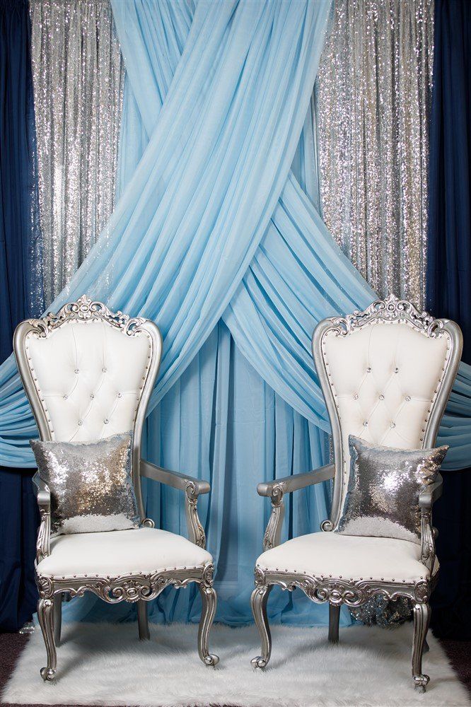 Two petite thrones with silver trim, silver accent pillows and a criss cross drape design in the background.