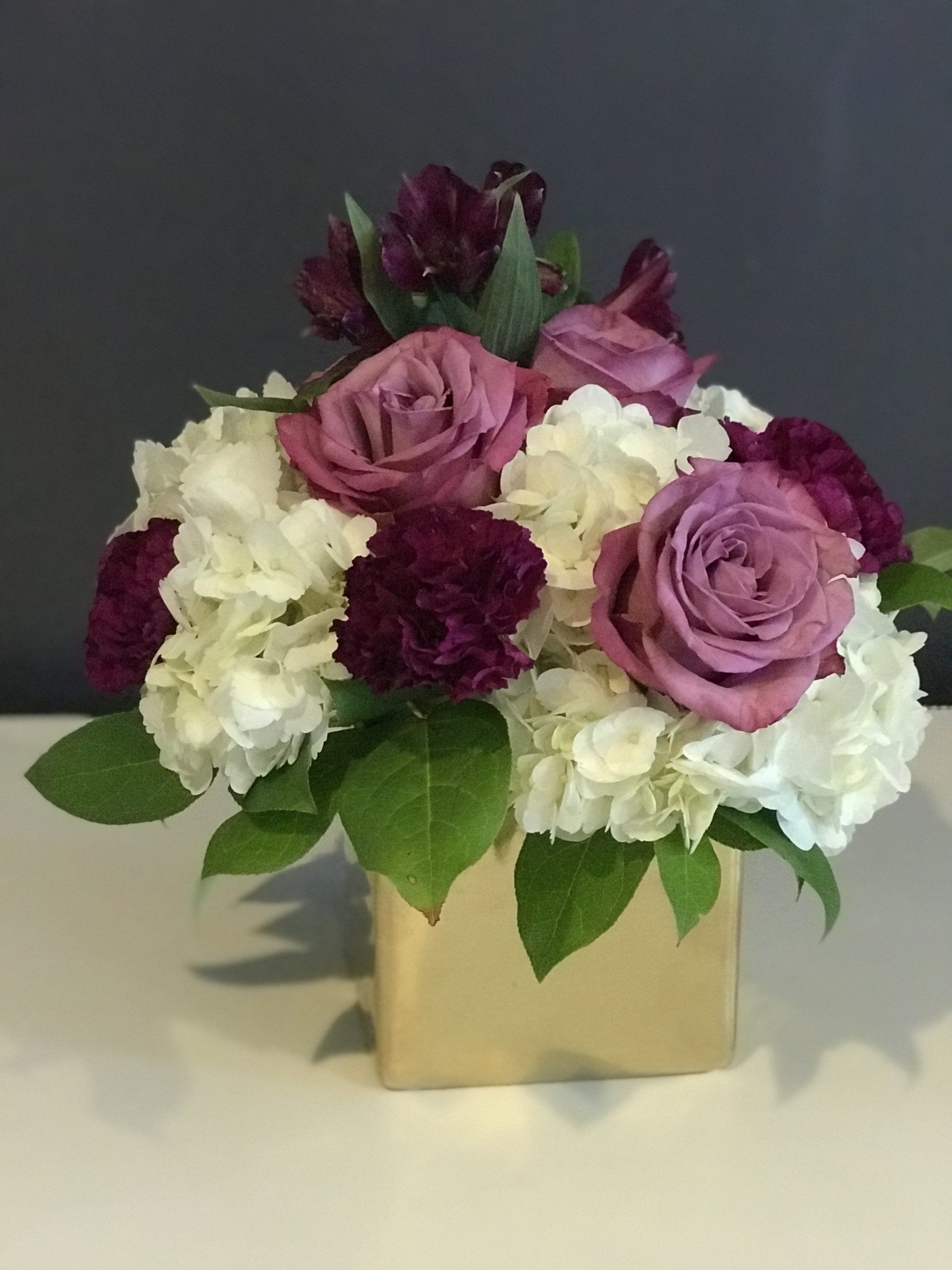 Close up of floral centerpiece in a gold cube vase.