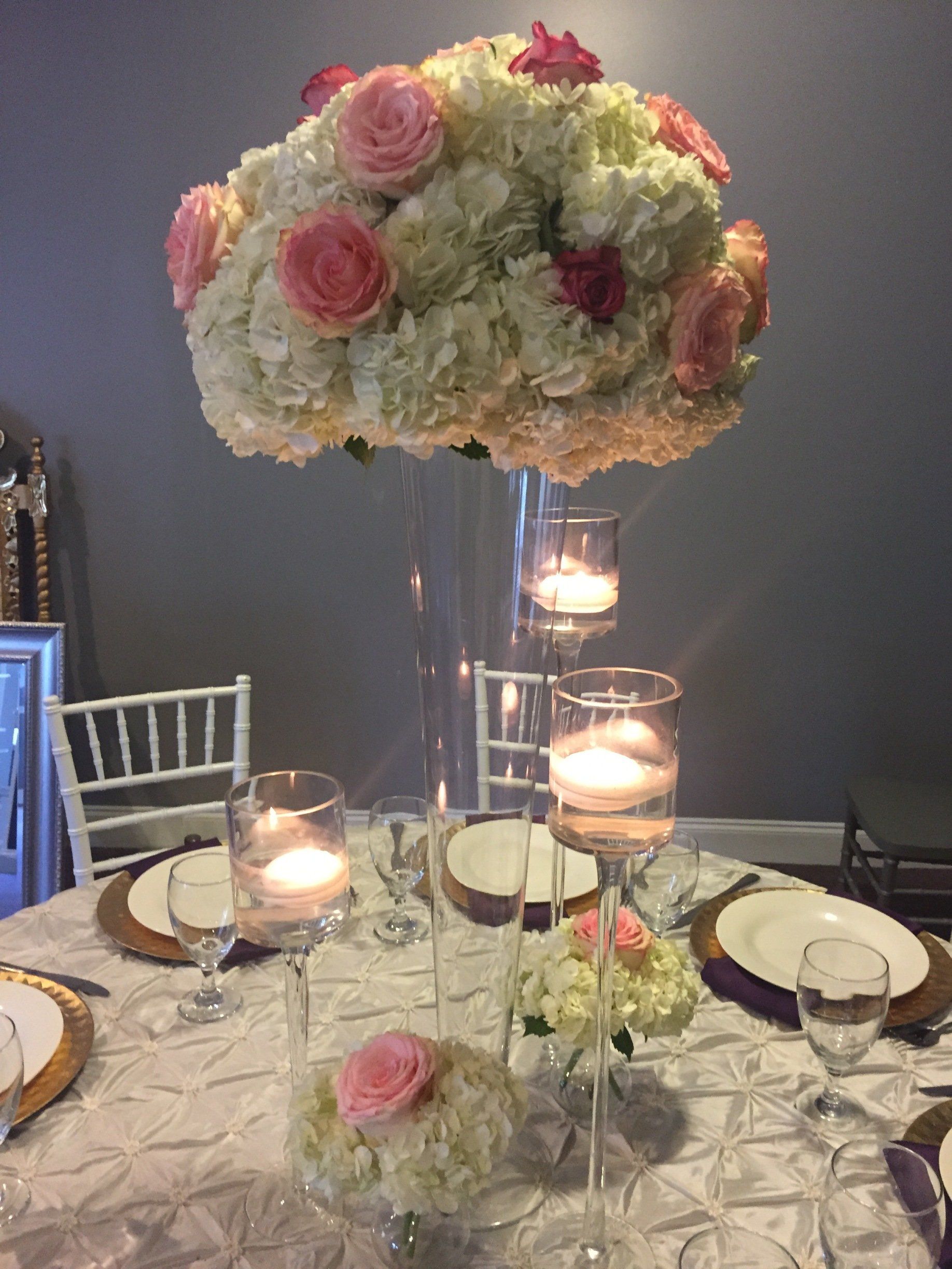 Elegant centerpiece design with a tall glass tapered cylinder with floral arrangement sitting on top, and tall stem floating candle holders.