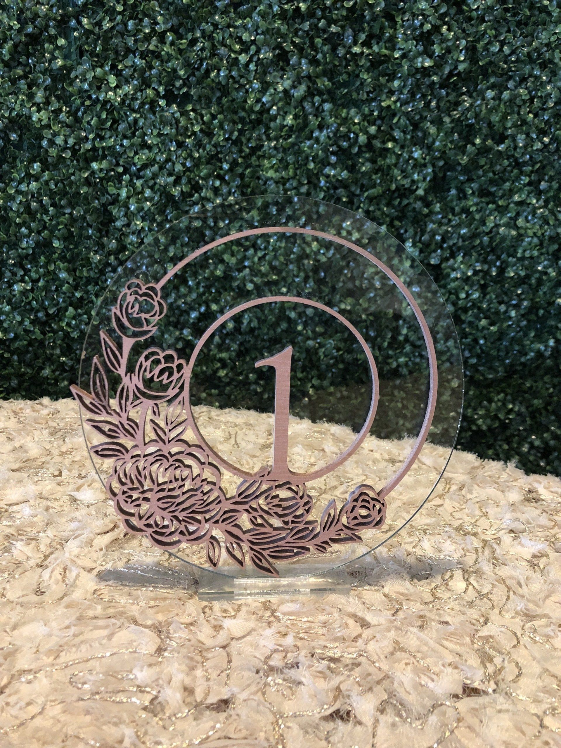 A laser cut circle design table number (with a 1 at the center) with an intricate flower design.