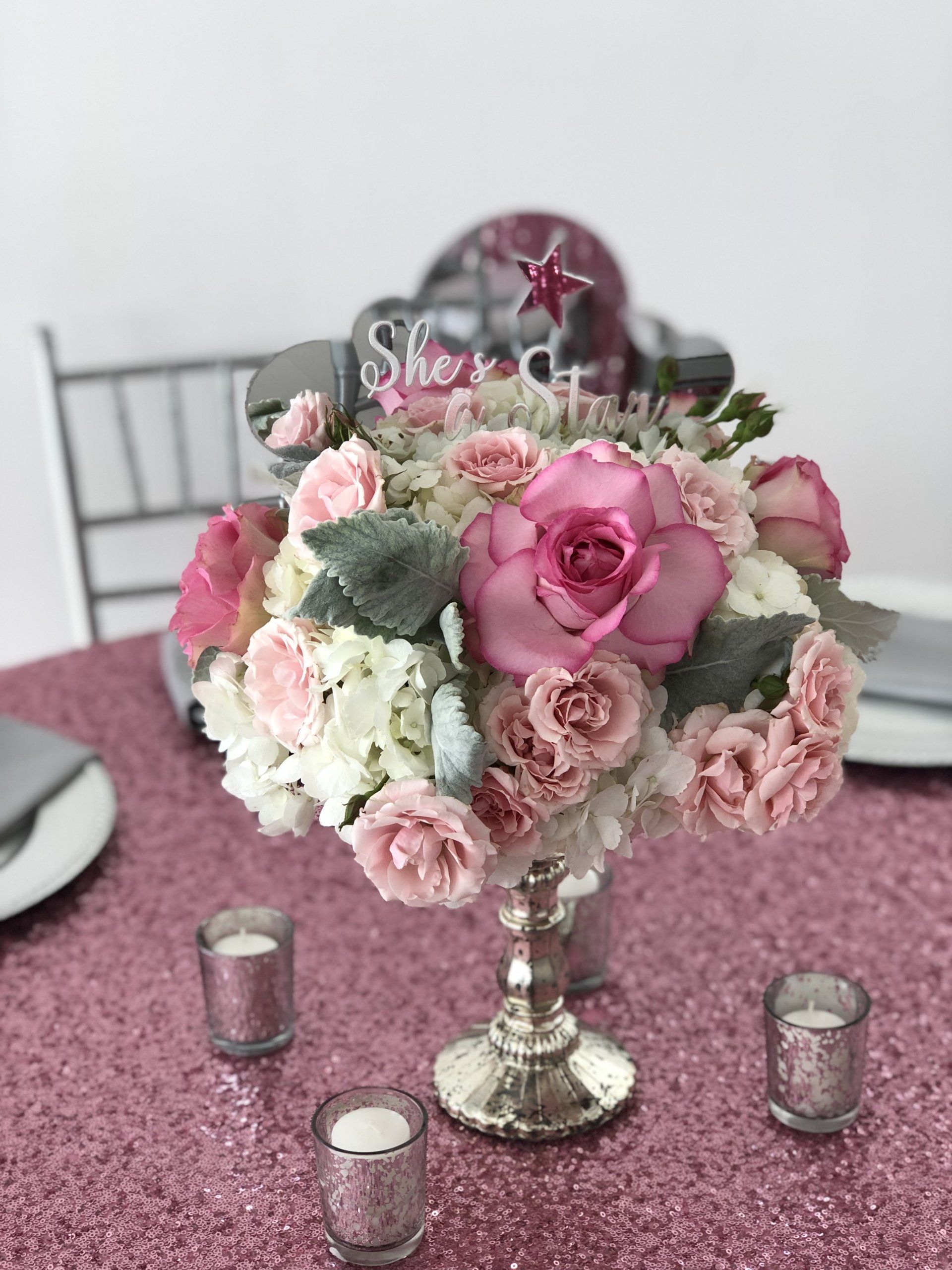 Multi flower centerpiece with cut out words and a star surrounded by tea light candles on a sequin pink table cloth.