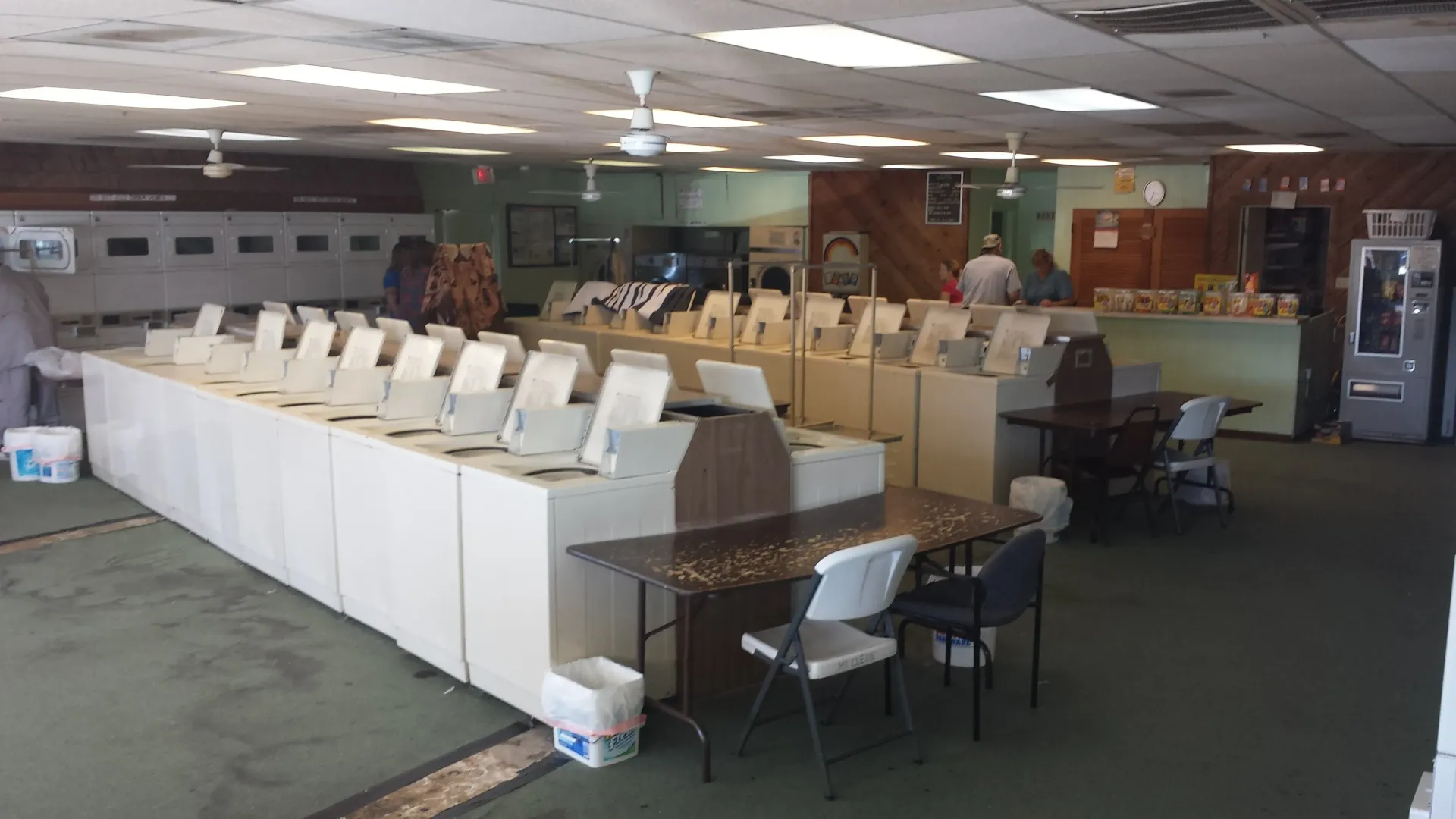 Interior of a laundromat with rows of washing machines. Tables, chairs, and vending machines are also visible.