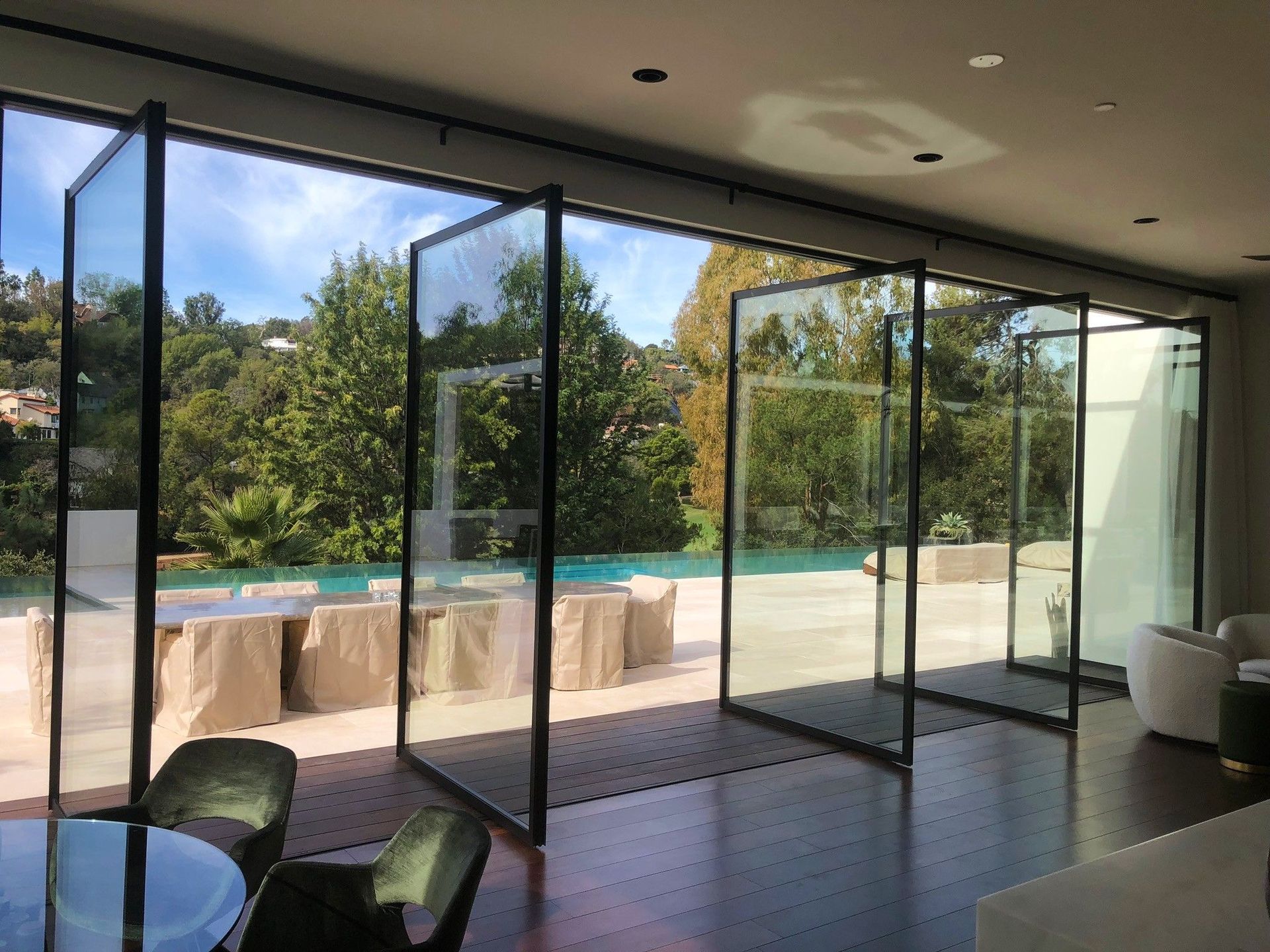 Large glass doors open to a backyard with a pool and lush greenery. The doors are black-framed and create a seamless indoor-outdoor transition.