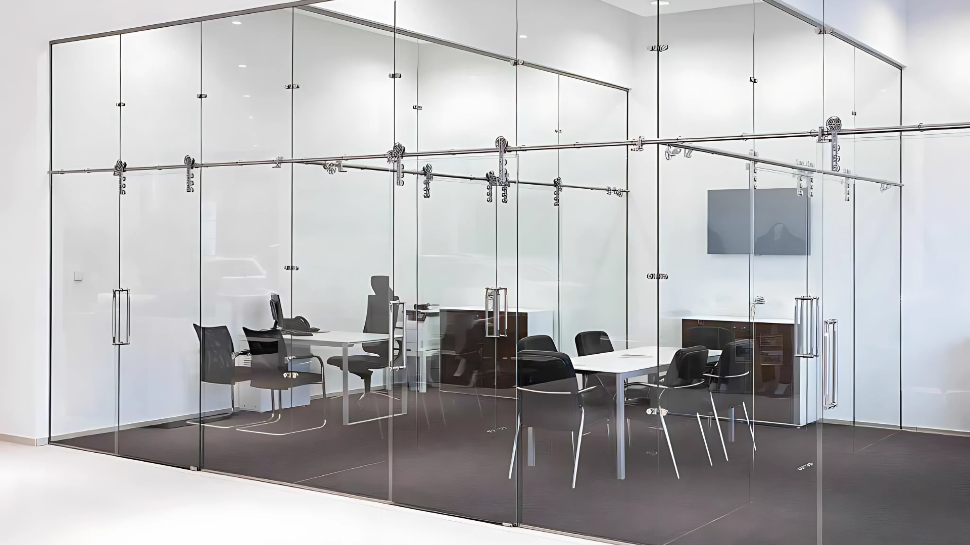 Glass-walled office space with a conference table and chairs, modern design, featuring transparent doors and metallic hardware.