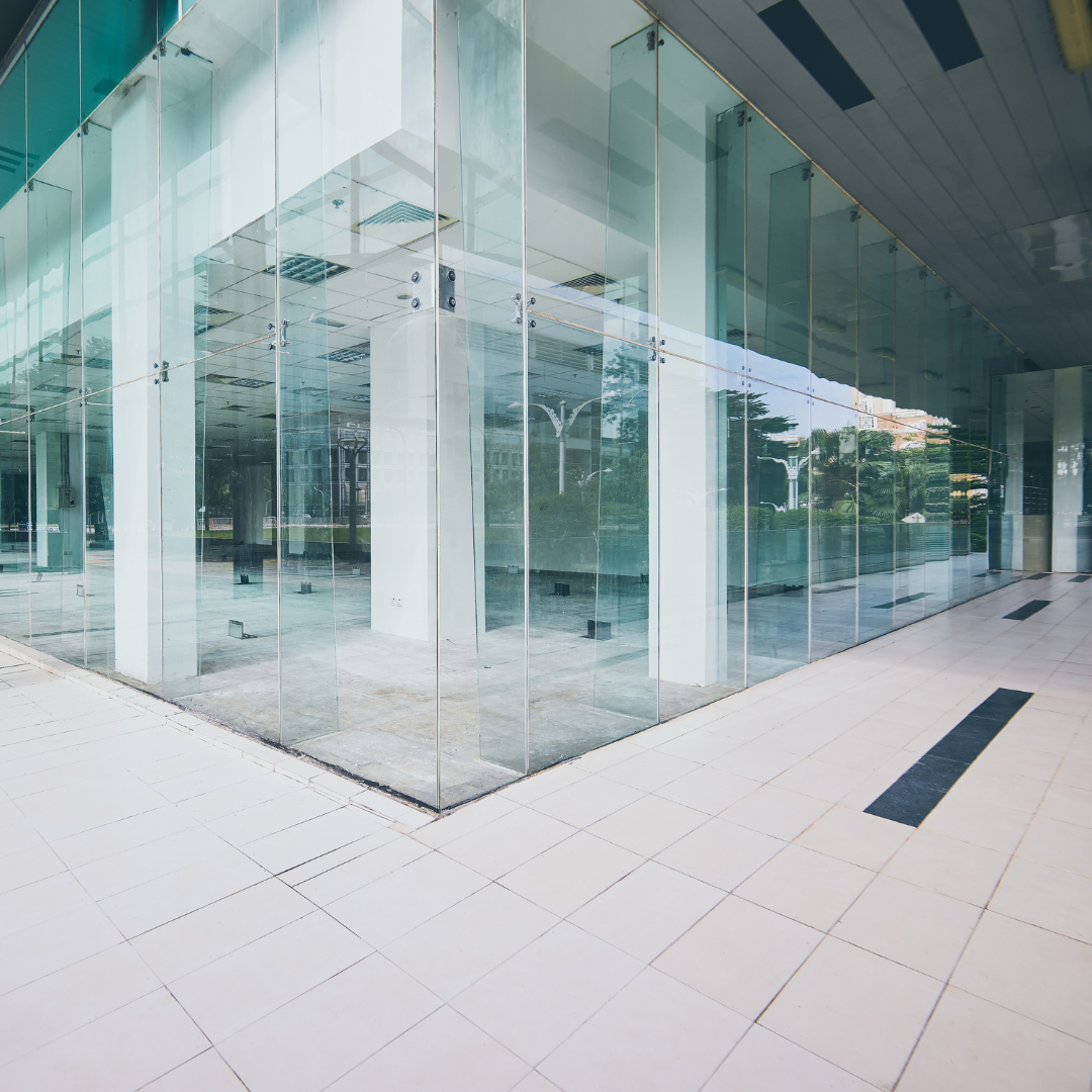Glass-walled building exterior with white tile floors, reflecting the surrounding environment, creating a modern aesthetic.