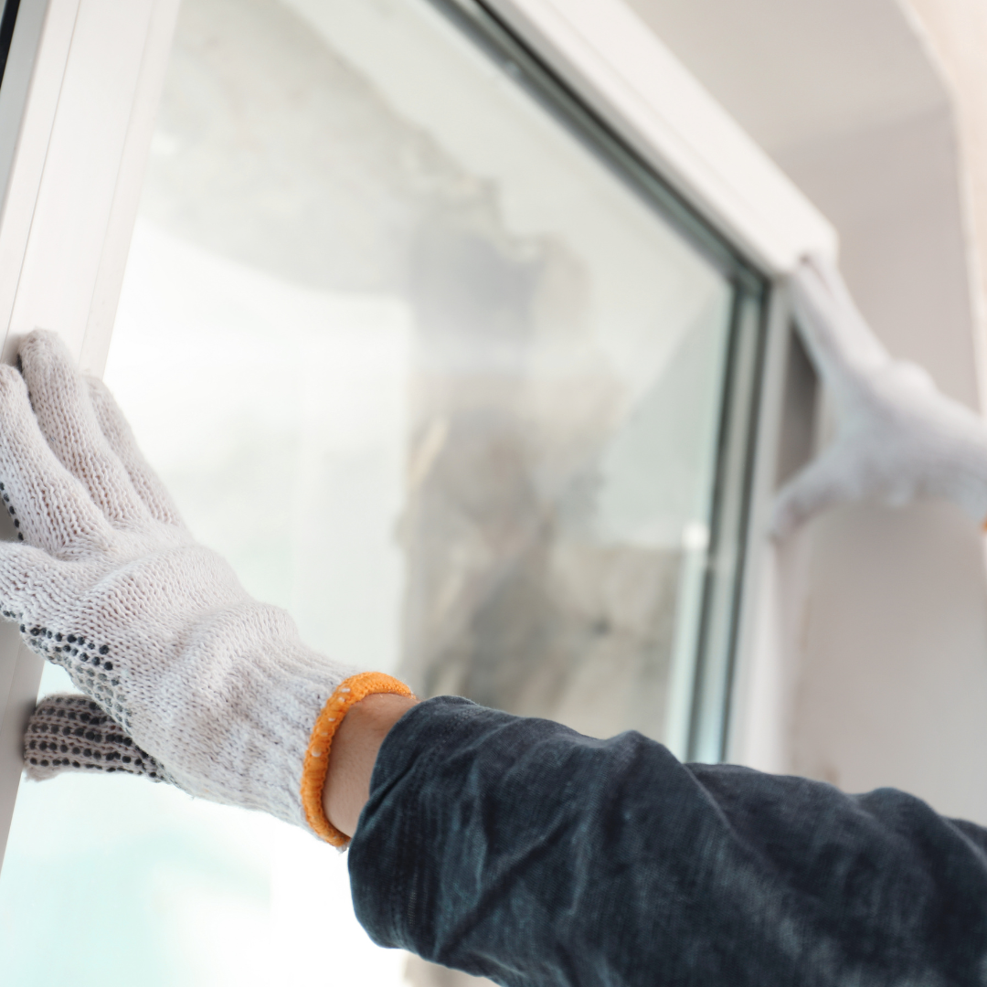 Person wearing gloves installing a window, hands on the frame.