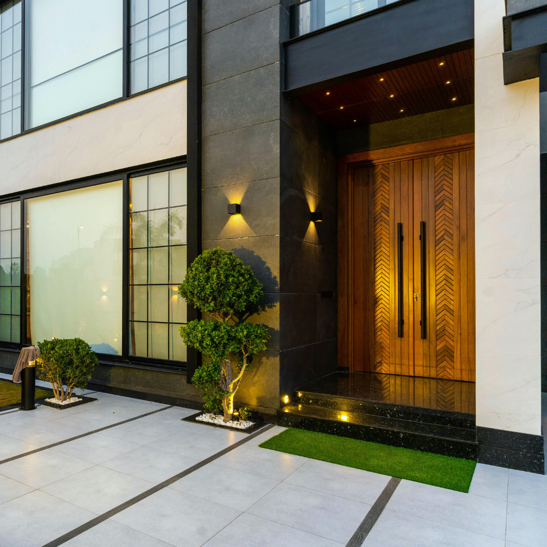 Modern home exterior with large wooden front doors, outdoor lighting, and manicured landscaping.