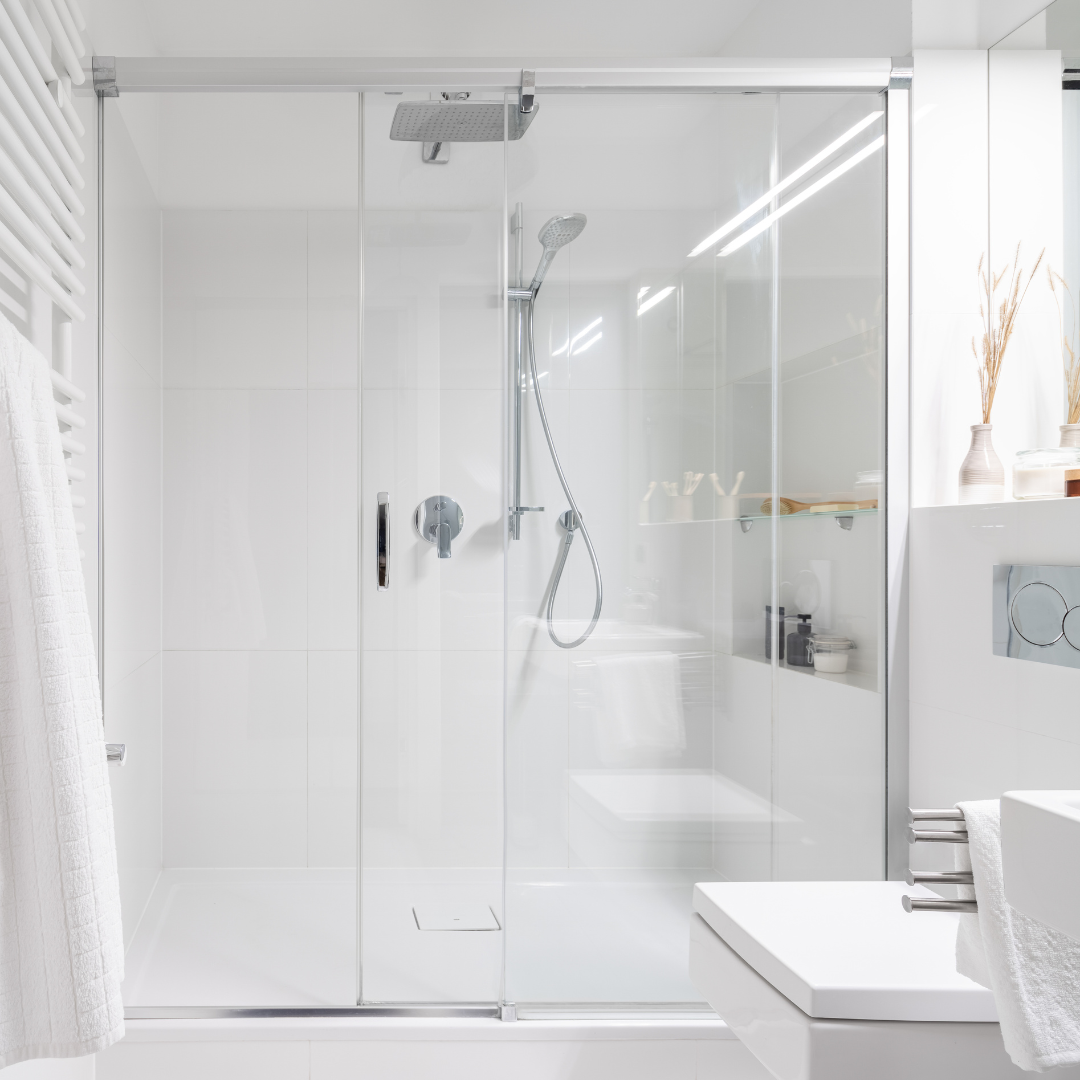 A modern, white bathroom with a glass-enclosed shower. A white towel hangs on the left.