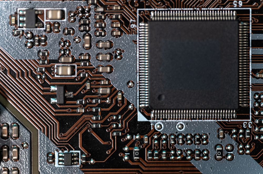 Close-up of a circuit board with a central microchip and various electronic components in shades of brown and gray.